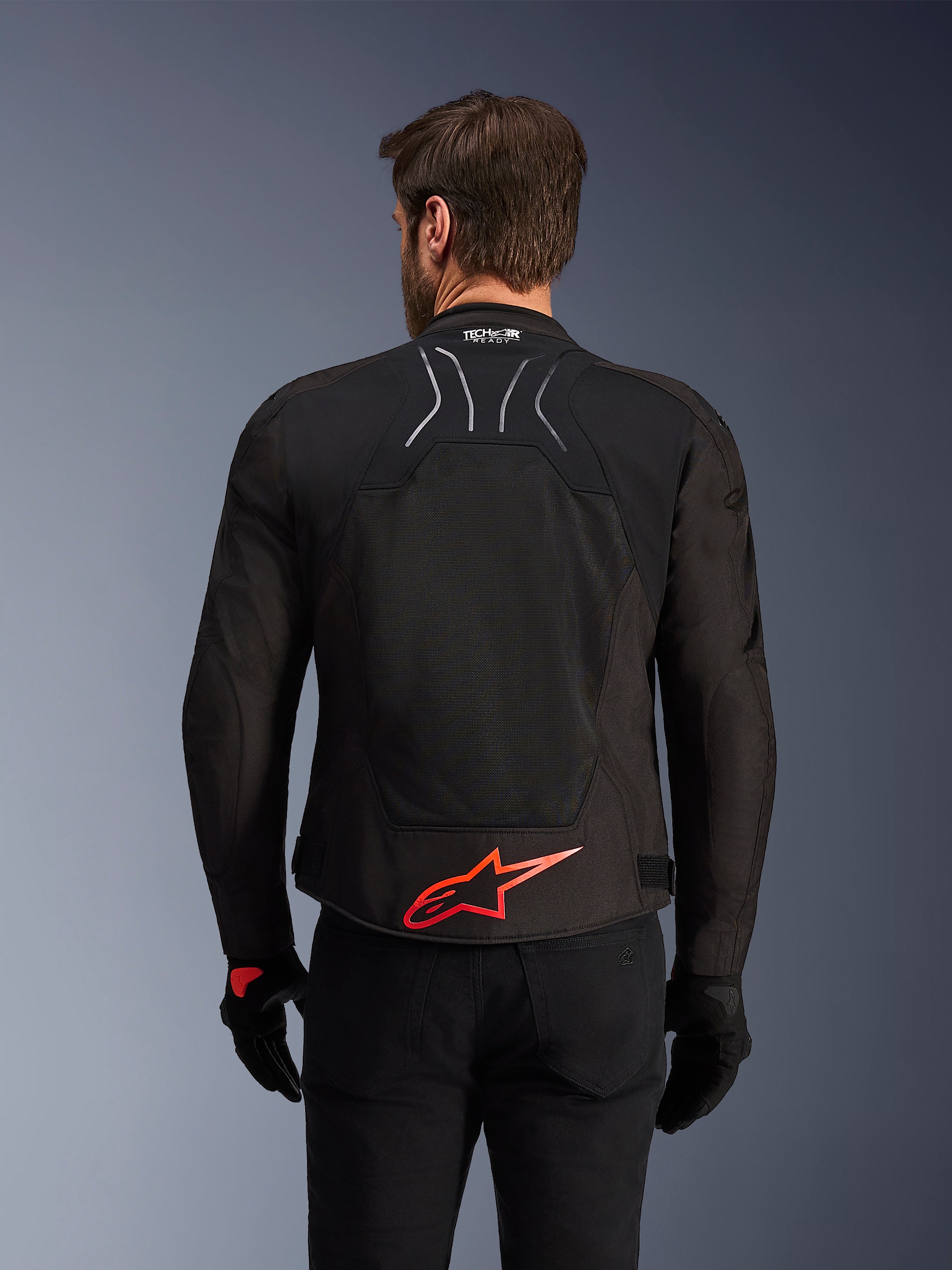 Alpinestars SMX Air Jacket, Rear View, Black with Bright Red Alpinestars logo on the lower back, featuring a high-airflow tech mesh panel and Tech-Air Ready branding, worn by a male rider with black pants and gloves