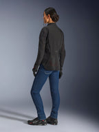 Woman wearing the Alpinestars Stella Aeroshell Airflow Jacket, Black Anthracite, rear three-quarter view showing breathable mesh panels and elongated rear profile, paired with blue denim riding jeans and black Alpinestars shoes