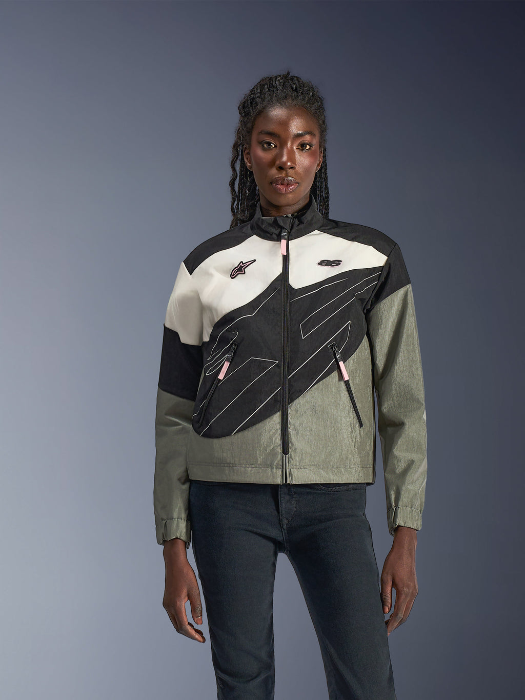 Woman wearing the Alpinestars Stella Moshell Jacket, urban motorcycle jacket in Black Fur Gray Off White and Pink, asymmetrical design with technical graphics, pink zipper pulls and Alpinestars logos, contemporary streetwear style for urban riders.