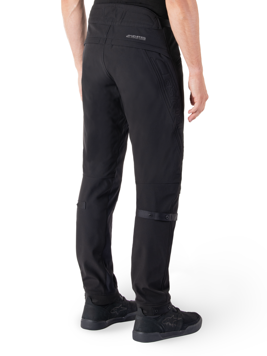 Alpinestars Alden Pants, Urban Motorcycle Pants, Black, rear view showing technical softshell fabric with quilted details, MO.ST.EQ. reflective branding on the back yoke, and adjustable calf straps, paired with black riding shoes