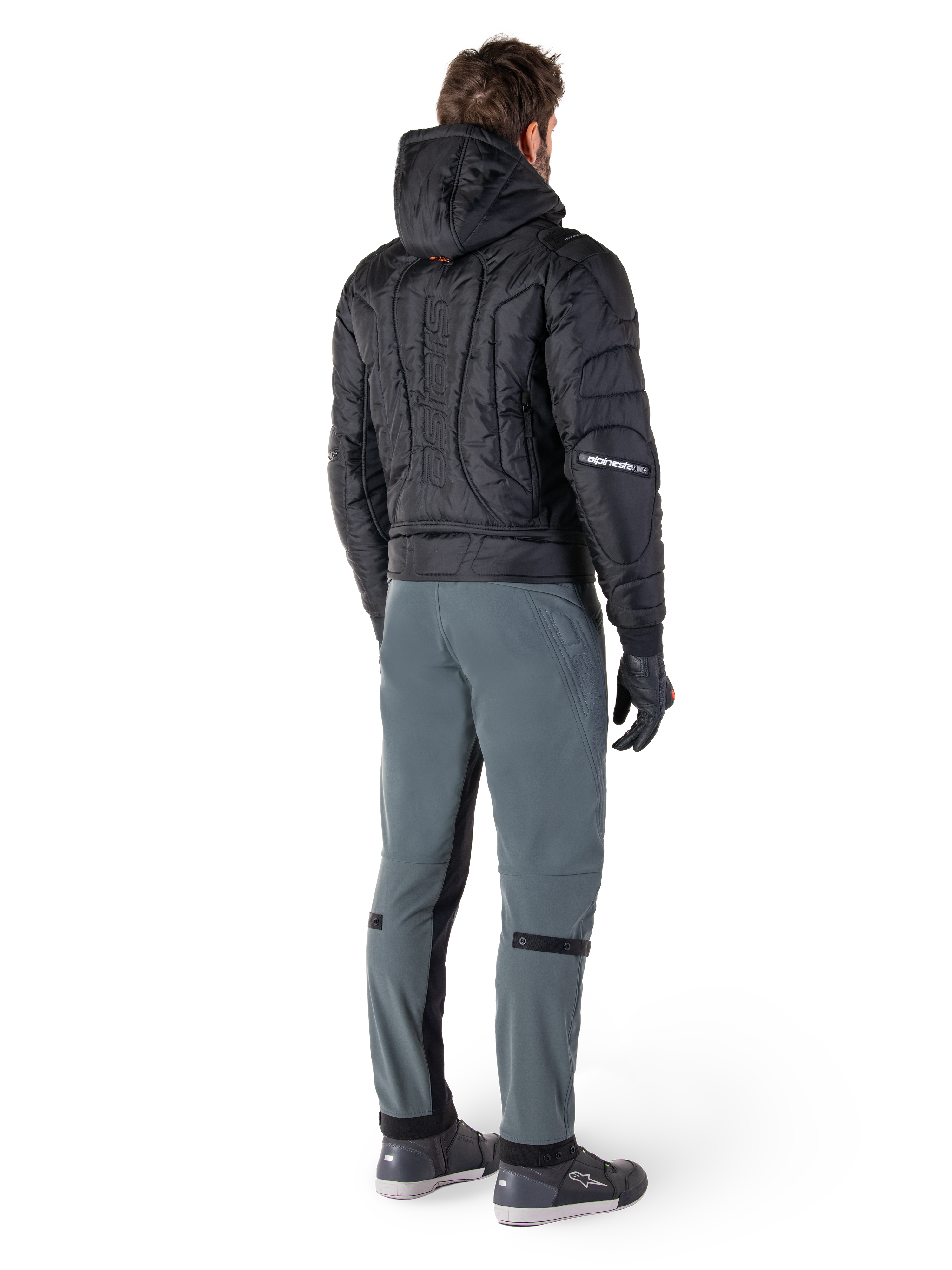 Alpinestars Alden Pants, urban motorcycle pants, Urban Gray, rear view of rider wearing a black quilted hooded jacket and riding sneakers, features slim fit below the knee with black stretch panels and knee adjusters, modern streetwear-inspired design.