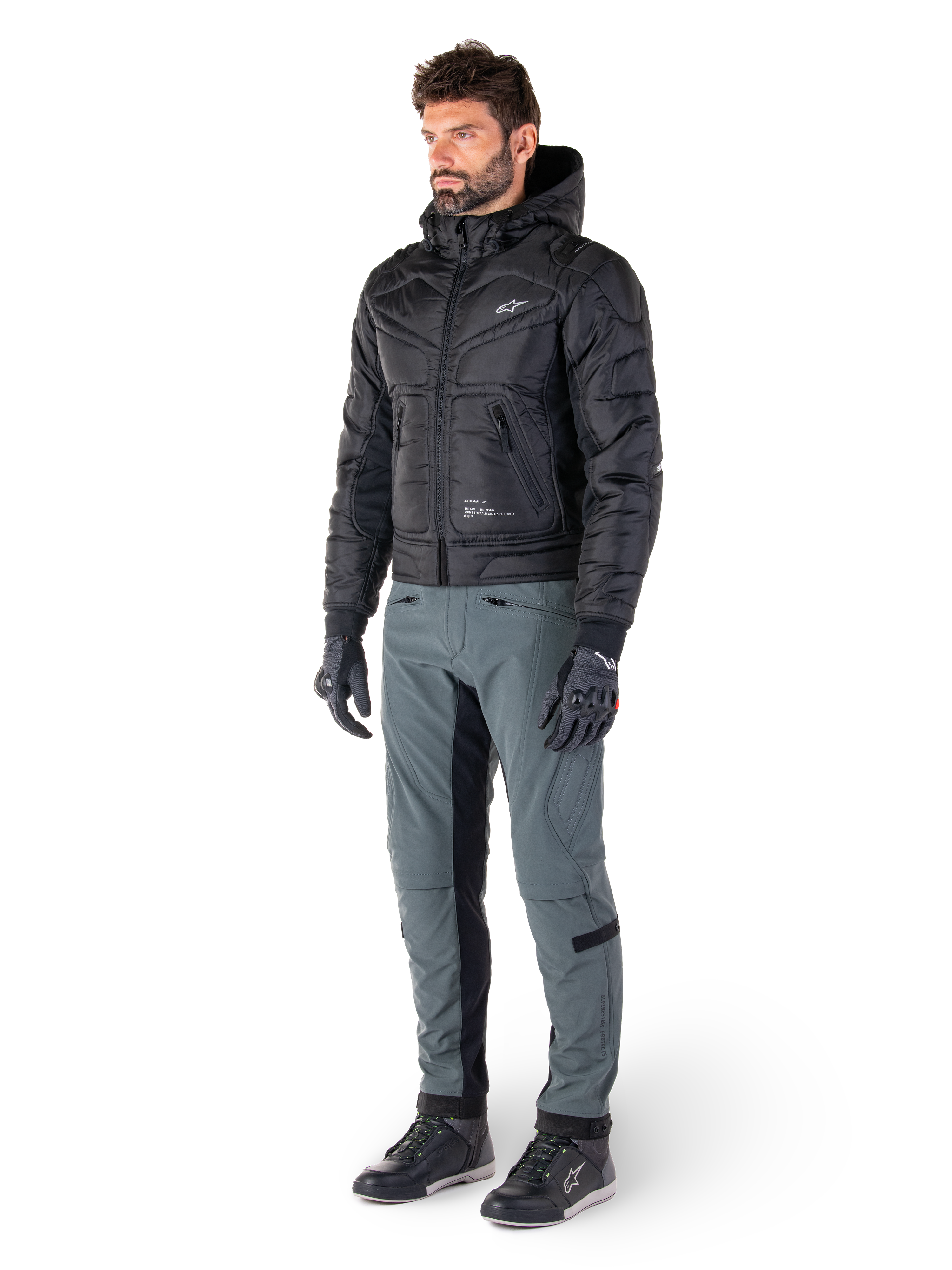 Alpinestars Alden Pants in Urban Gray, worn by a model with a black quilted hooded jacket, gloves, and riding shoes, featuring quilted detailing on the sides and black inner leg panels, streetwear-inspired urban motorcycle gear.