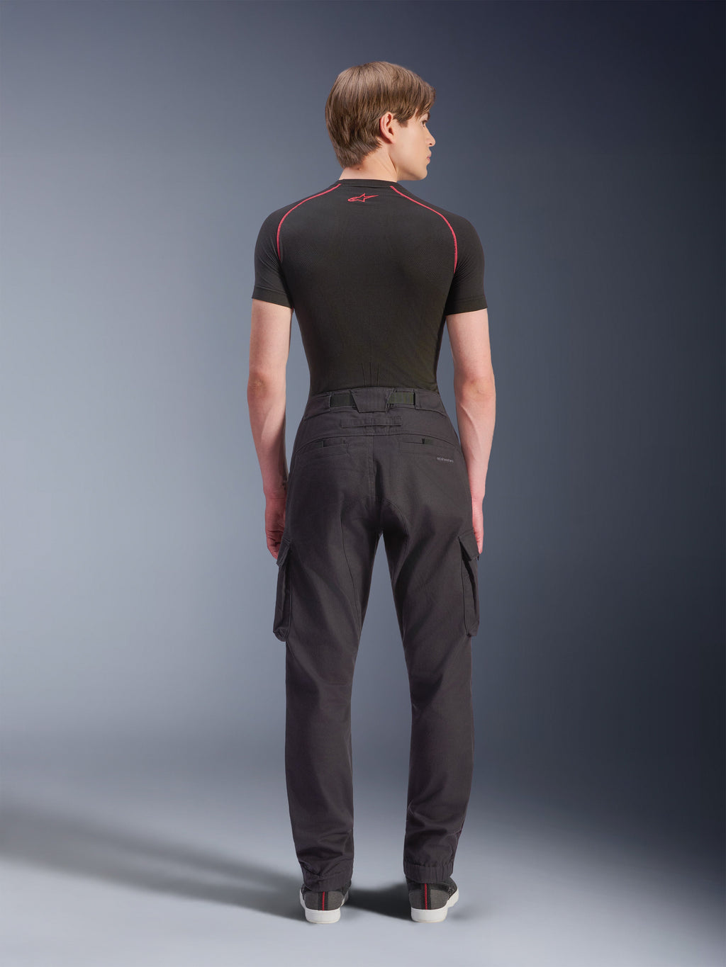 Alpinestars Flex-AST Cargo Pants, Motorcycle Cargo Pants, Black, rear view on model, featuring a regular tapered fit with elasticated hems and side cargo pockets, styled with a black base layer and casual sneakers