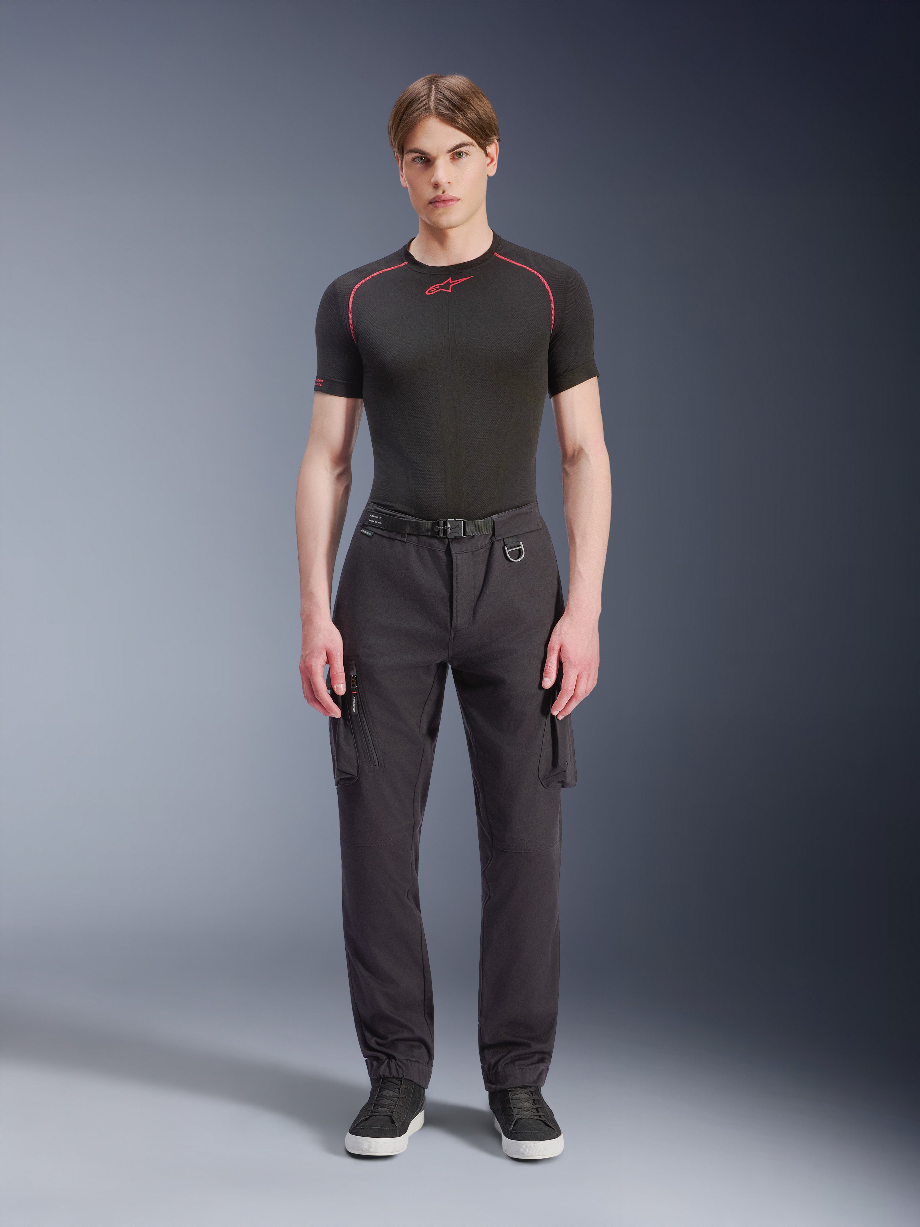 Alpinestars Flex-AST Cargo Pants - Short, Black, worn by a male model with a black performance t-shirt and black sneakers, urban motorcycle pants featuring multiple cargo pockets, a tapered fit, and a built-in belt with buckle and D-ring