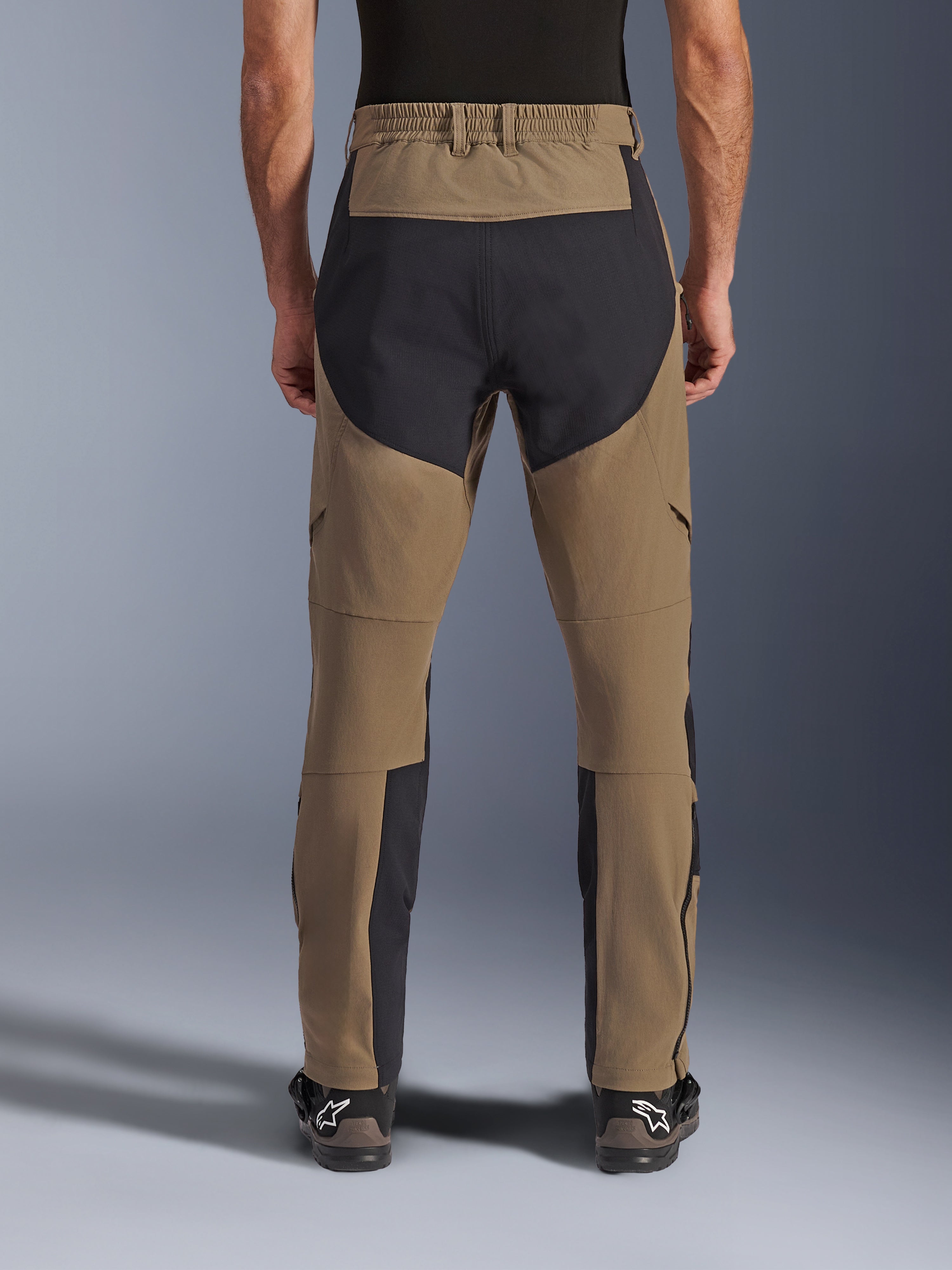 Alpinestars Flex-AST Explorer Pants, Adventure Motorcycle Pants, Walnut Black, rear view worn by rider, black ripstop reinforcement panels on the seat and inner legs, elasticated waistband, long lower leg zippers, and matching adventure boots