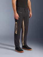 Alpinestars Flex-AST Canvas Pants, Urban Motorcycle Pants, Black Aluminum, featuring tan side panels with a vertical Alpinestars logo, workwear-inspired design with zippered pockets and ergonomic cut, worn with casual black sneakers for a modern city look.