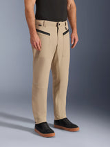 Alpinestars Flex-AST Canvas Pants, urban motorcycle pants in tan brown, monolayer stretch polycotton with workwear styling, featuring zippered front pockets and tapered legs, worn with a black t-shirt and black sneakers, casual protective gear for city riding
