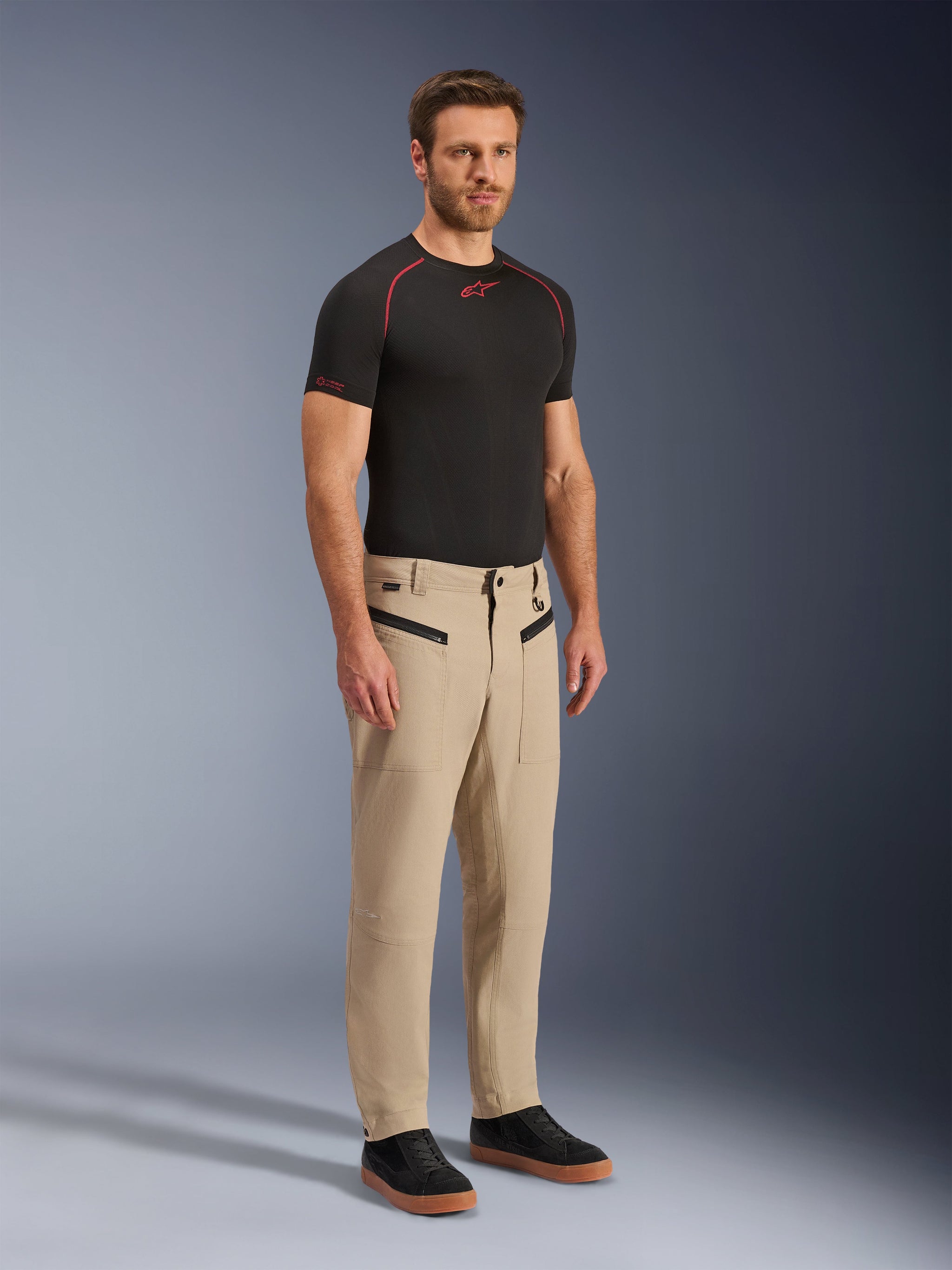 Alpinestars Flex-AST Canvas Pants, Urban Motorcycle Pants, Brown, full-body studio shot of a man wearing the pants with a black performance t-shirt and black sneakers, featuring heritage workwear styling, zippered front pockets, and a durable polycotton twill construction.