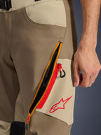 Alpinestars Maxdura Dual Pants, Walnut and Aluminum, close-up of thigh detail featuring a large diagonal zippered ventilation system with red accents and a red Alpinestars logo on a tan panel, adventure motorcycle gear