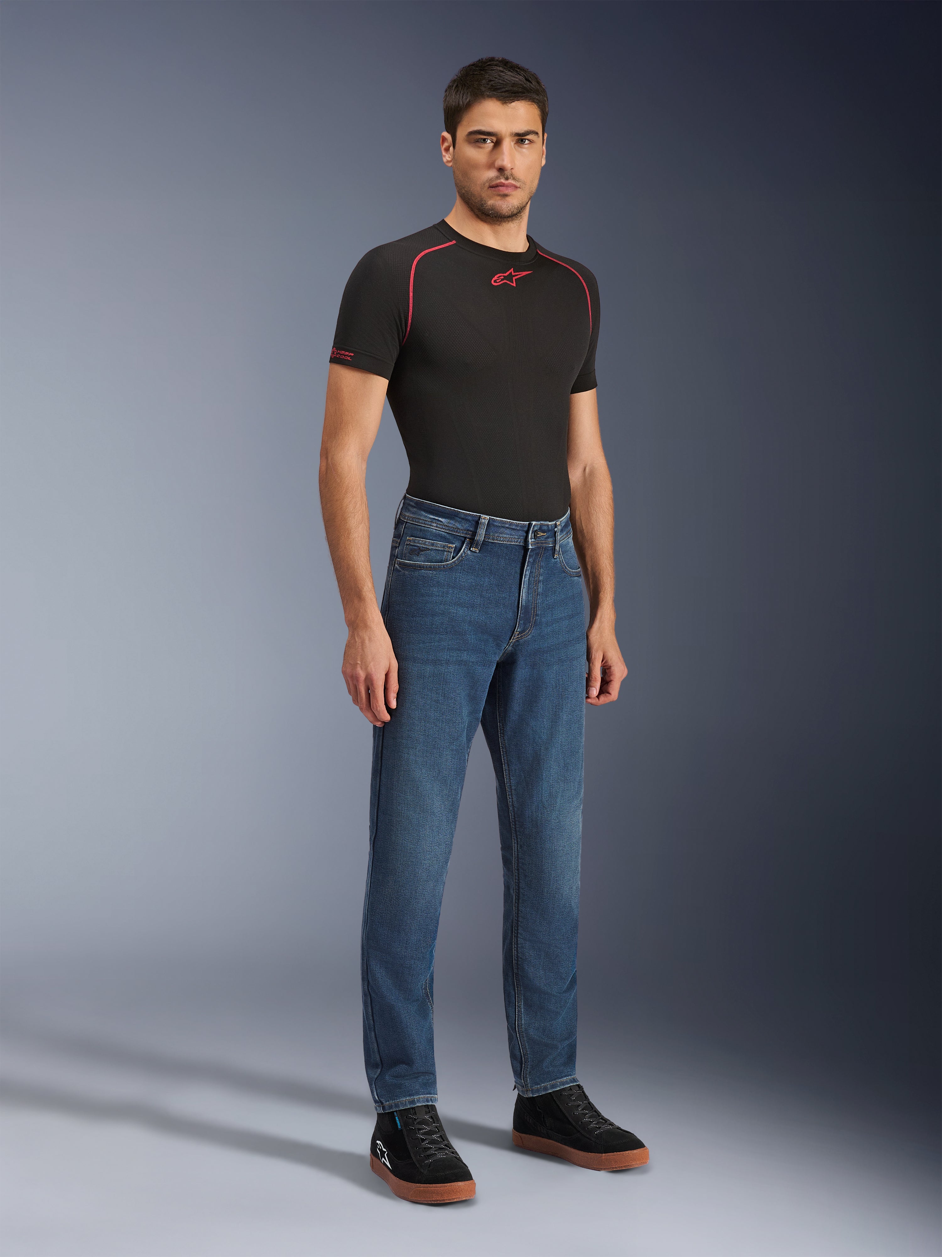 Alpinestars Flex-AST 5 Denim Pants, Indigo Washed motorcycle jeans, modern tapered fit, worn by a male model with a black performance t-shirt and black sneakers, casual urban riding apparel.