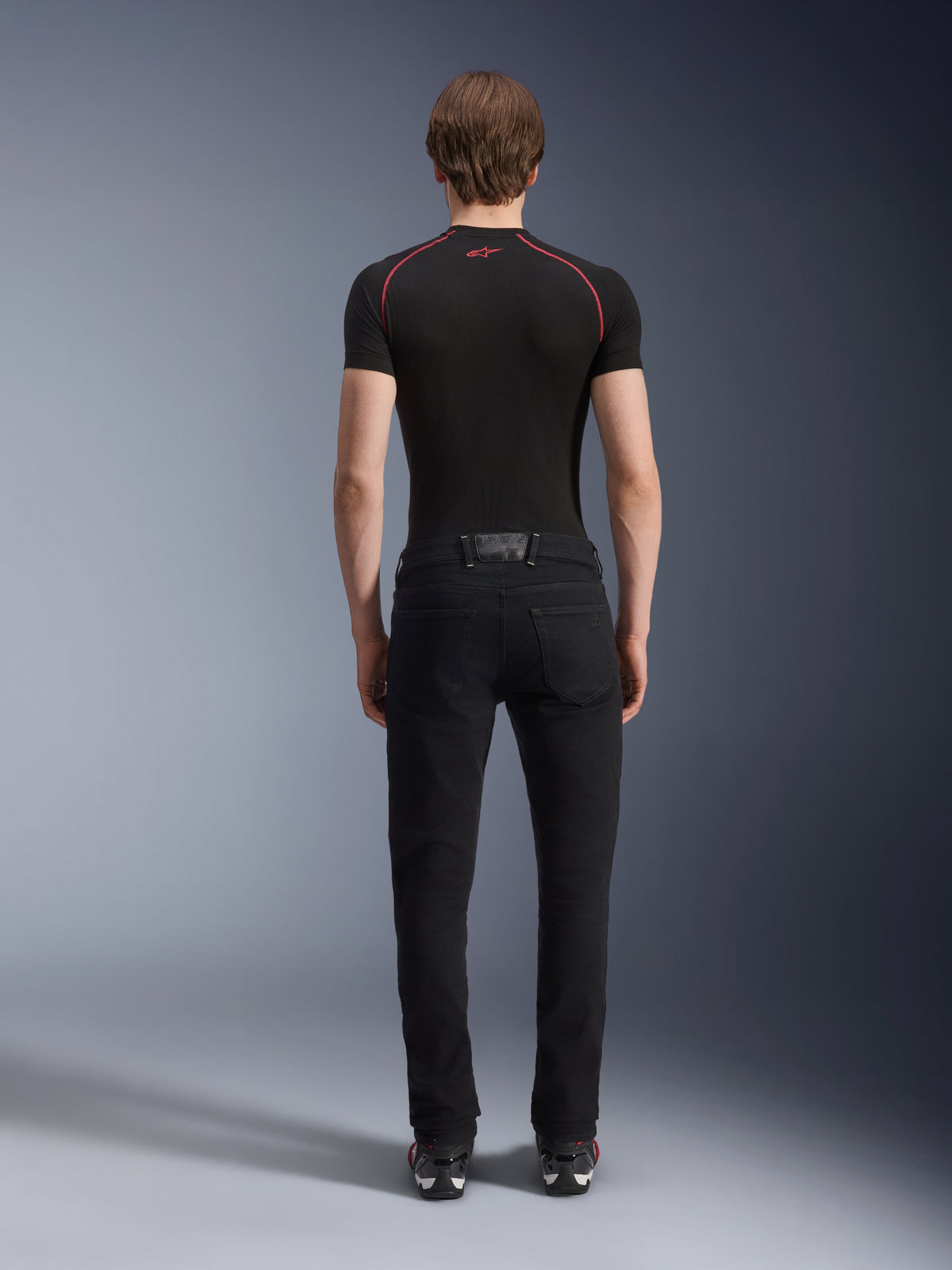 Alpinestars Copper V3 Denim Pants in Black Rinse, rear view on a model, regular straight-leg motorcycle riding jeans made from stretch denim, paired with a black short-sleeved compression shirt and riding shoes, urban riding gear