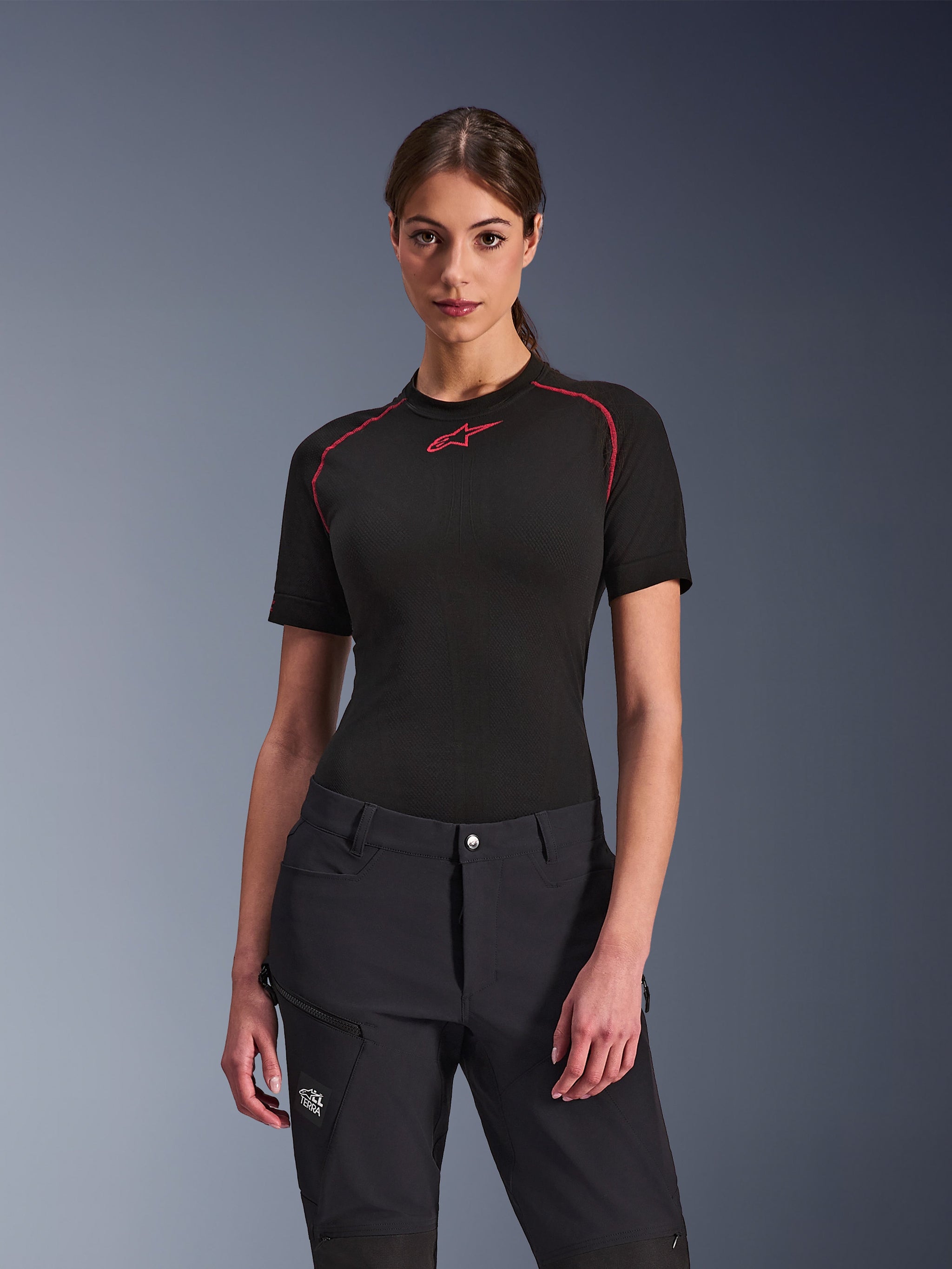 Woman wearing Alpinestars Stella Flex-AST Explorer Pants in Black, paired with a black short-sleeve base layer with red accents, adventure riding apparel featuring cargo pockets and All Terra branding