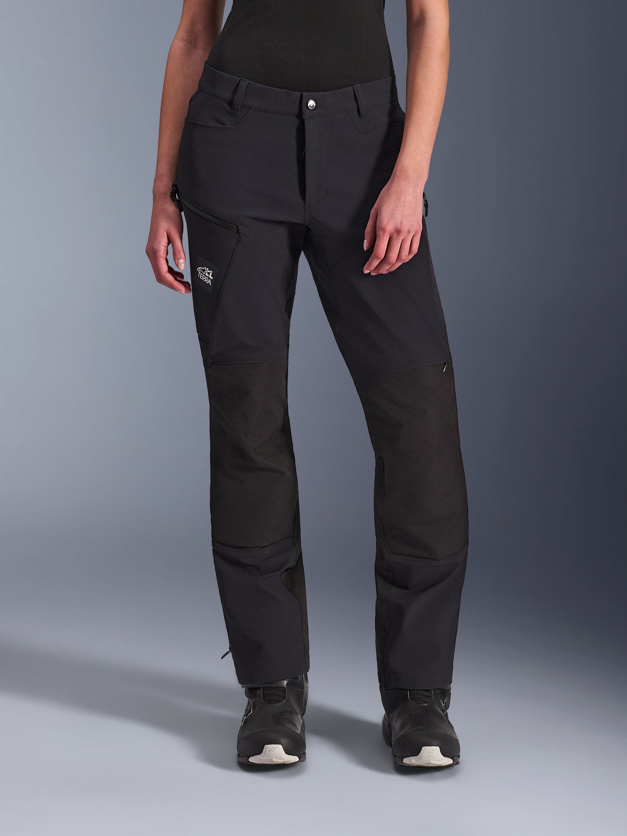 Alpinestars Stella Explore AST Pants, Women's Motorcycle Adventure Pants, Black, featuring ripstop reinforcements at the knees, zippered cargo pocket on the thigh, and 'Terra' logo, worn with black boots, streamlined design for adventure touring and road riding.