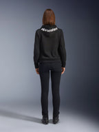 Daisy V3 Women's Riding Denim, Black Rinse, slim fit motorcycle pants, rear view showing high back waist and feminine silhouette, paired with a black Alpinestars hoodie and black riding boots, urban casual riding gear