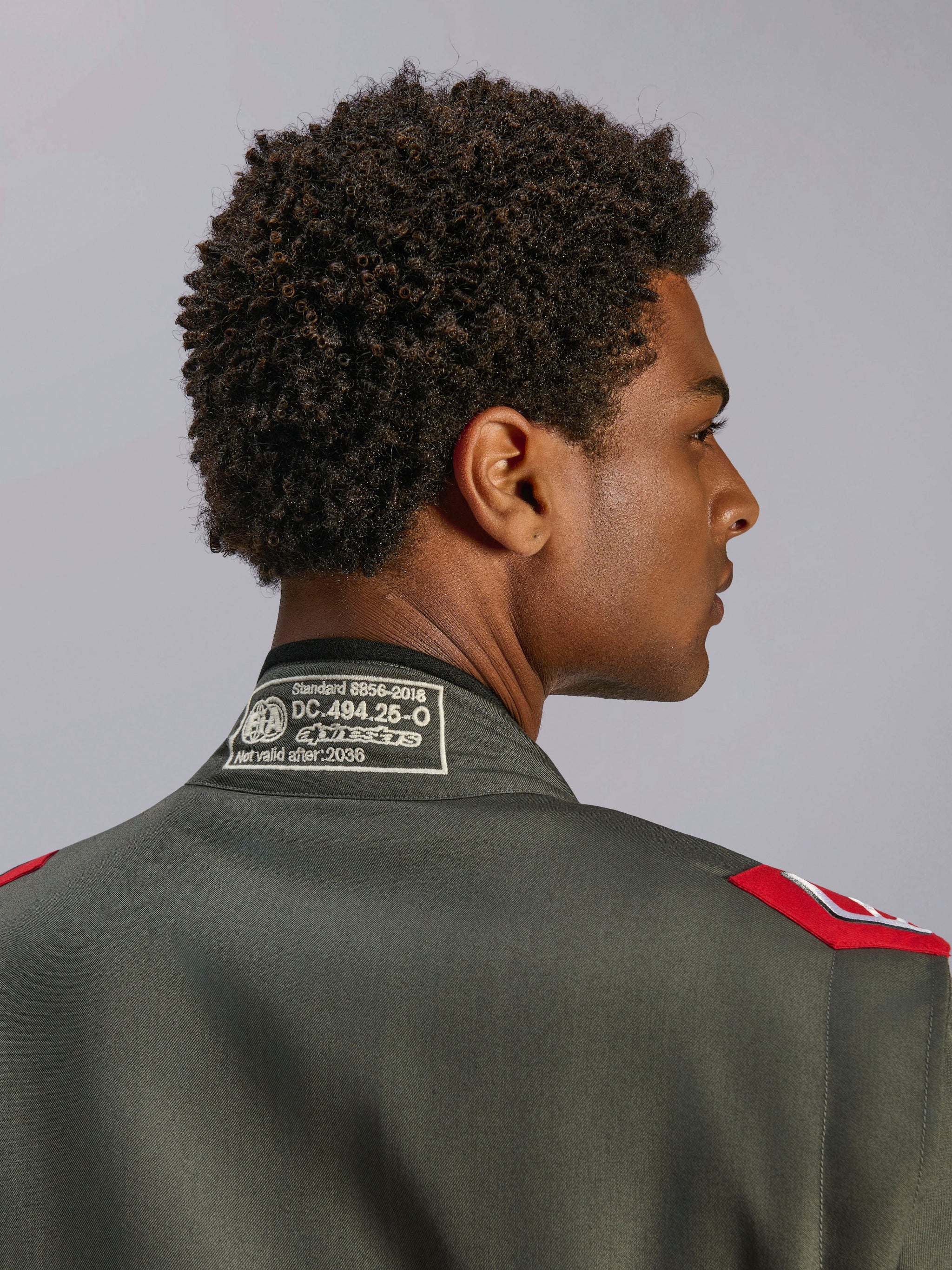 Alpinestars GP Race V3 Suit FIA, Anthracite Red racing suit, close-up of back collar showing FIA 8856-2018 certification label and red shoulder epaulettes, detailed view of professional motorsport apparel.