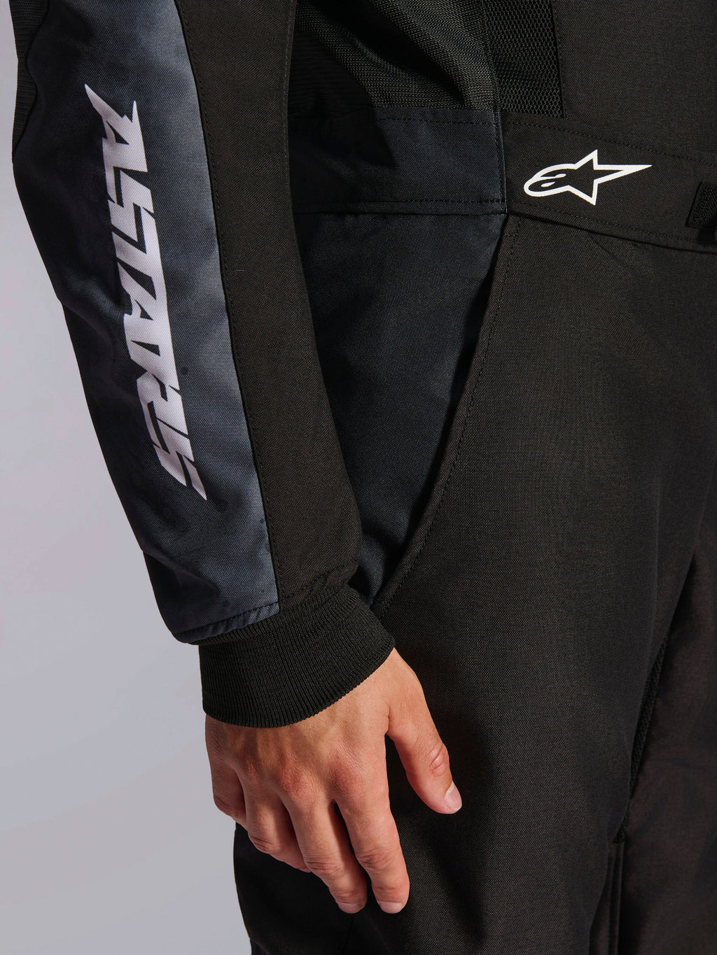 Alpinestars KMX-5 V3 Suit, Karting Suit, Black and Dark Shadow, close-up detail of side hip and arm, white ASTARS branding on the sleeve, white logo on the waist, featuring mesh panels for ventilation and a knitted wrist cuff