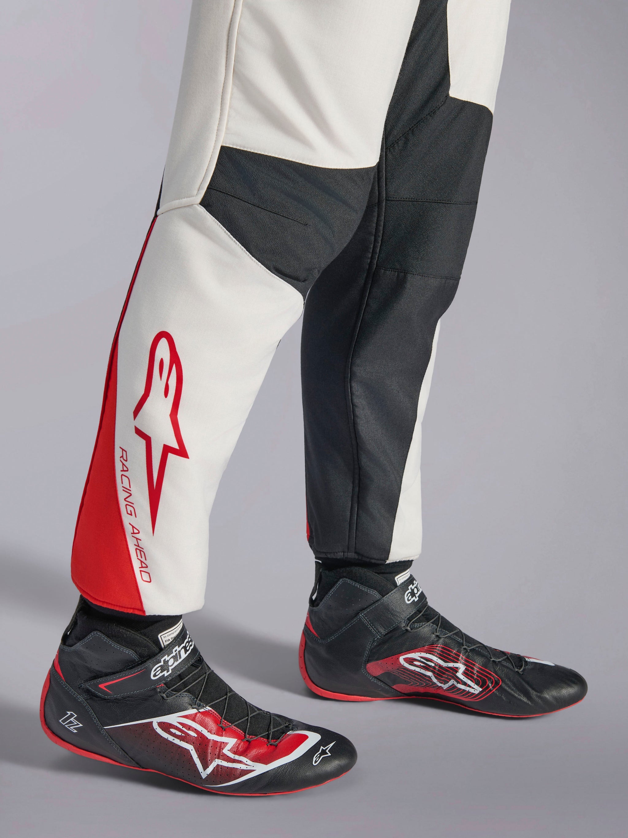 Alpinestars GP Tech V4 Suit, Auto Racing Suit, White Black and Red, lower leg view featuring white and black panels with red accents and 'RACING AHEAD' branding, worn with black racing shoes, professional motorsports gear