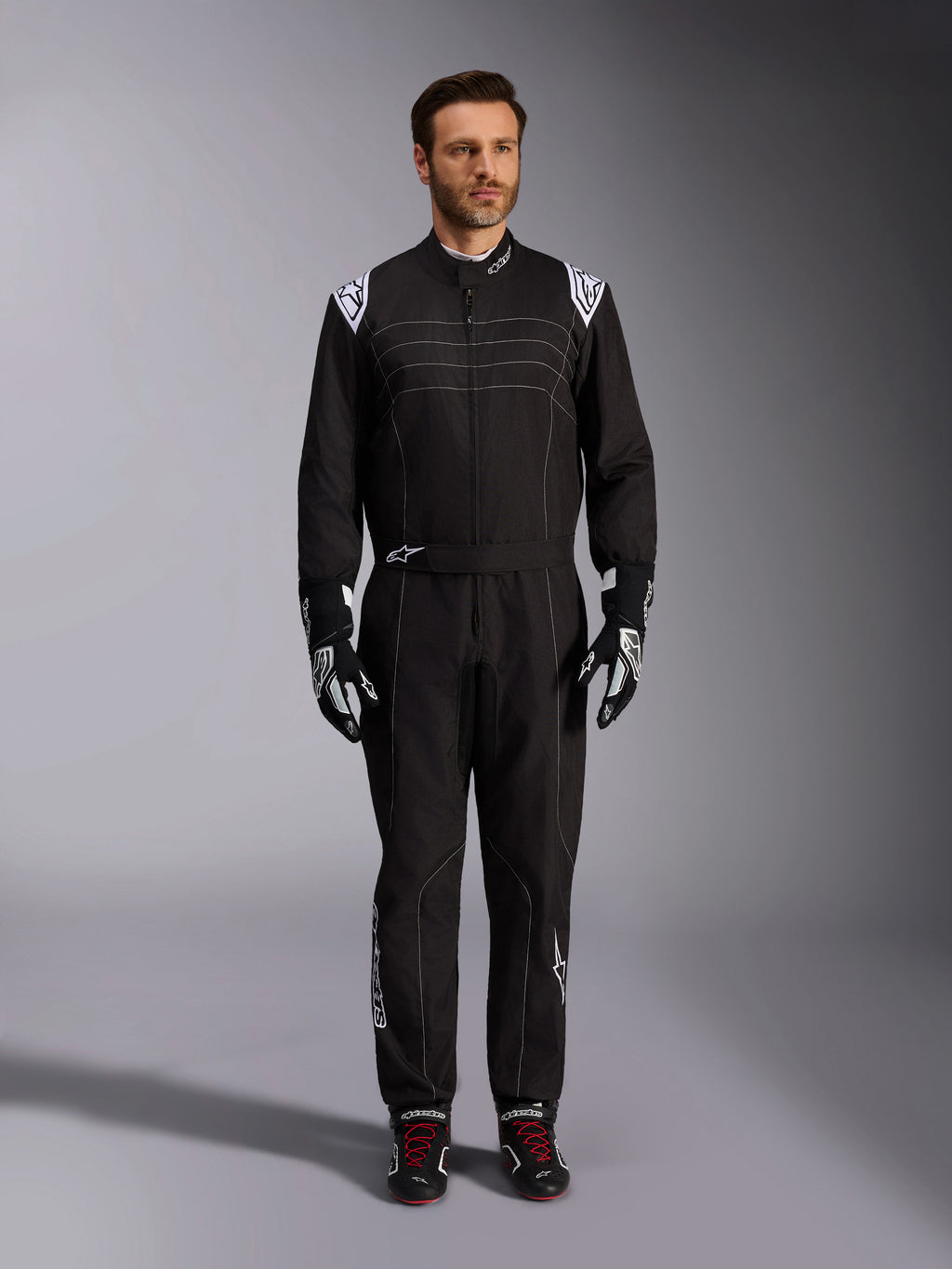 Alpinestars KMX-9 V3 Suit, Black and White Karting Suit, full-length view on a model, featuring white shoulder logos and accents, styled with black and white racing gloves and black shoes with red laces, athletic-regular fit for professional karting gear.