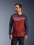 Male model wearing Alpinestars Maxdura Dual Jersey, Rust Brown and Navy Blue adventure motorcycle jersey, featuring dual zippered chest pockets, horizontal chest stripe with branding, technical mesh torso, and durable woven sleeves.