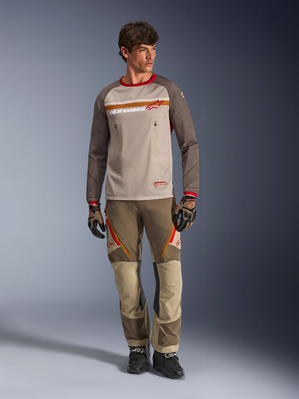 Alpinestars Maxdura Dual Jersey in Aluminum Walnut, adventure motorcycle jersey with tan mesh torso and brown sleeves, featuring red collar and horizontal chest stripe with Alpinestars logo, worn with matching adventure pants and gloves.