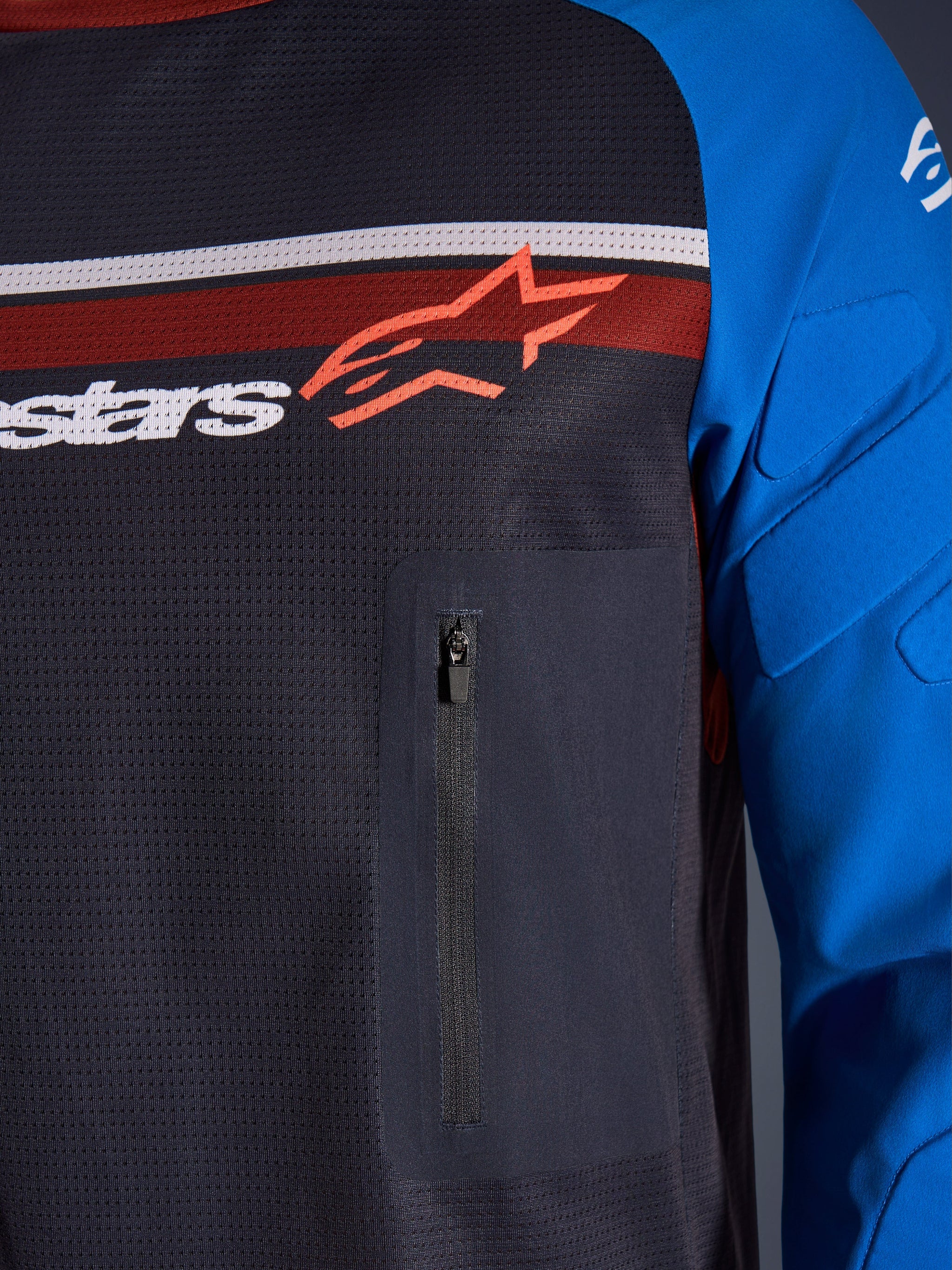 Alpinestars Maxdura Dual Jersey, close-up of chest and sleeve, Deep Gray and Royal Blue, featuring a zippered chest pocket, breathable mesh torso, and integrated padding on the sleeves, branded with the Alpinestars logo over red and white stripes.