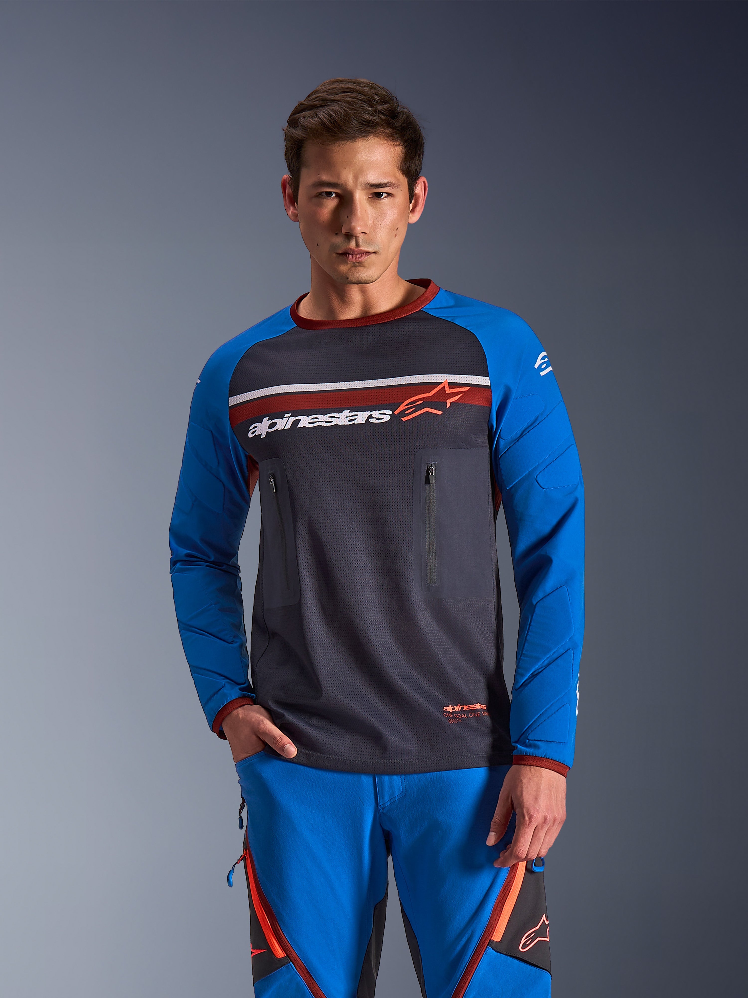 Alpinestars Maxdura Dual Jersey, Long-Sleeve Motorcycle Jersey, Deep Gray and Royal Blue with red accents, features zippered chest pockets and padded sleeves, worn with matching blue pants, technical apparel for adventure and dual-sport riding