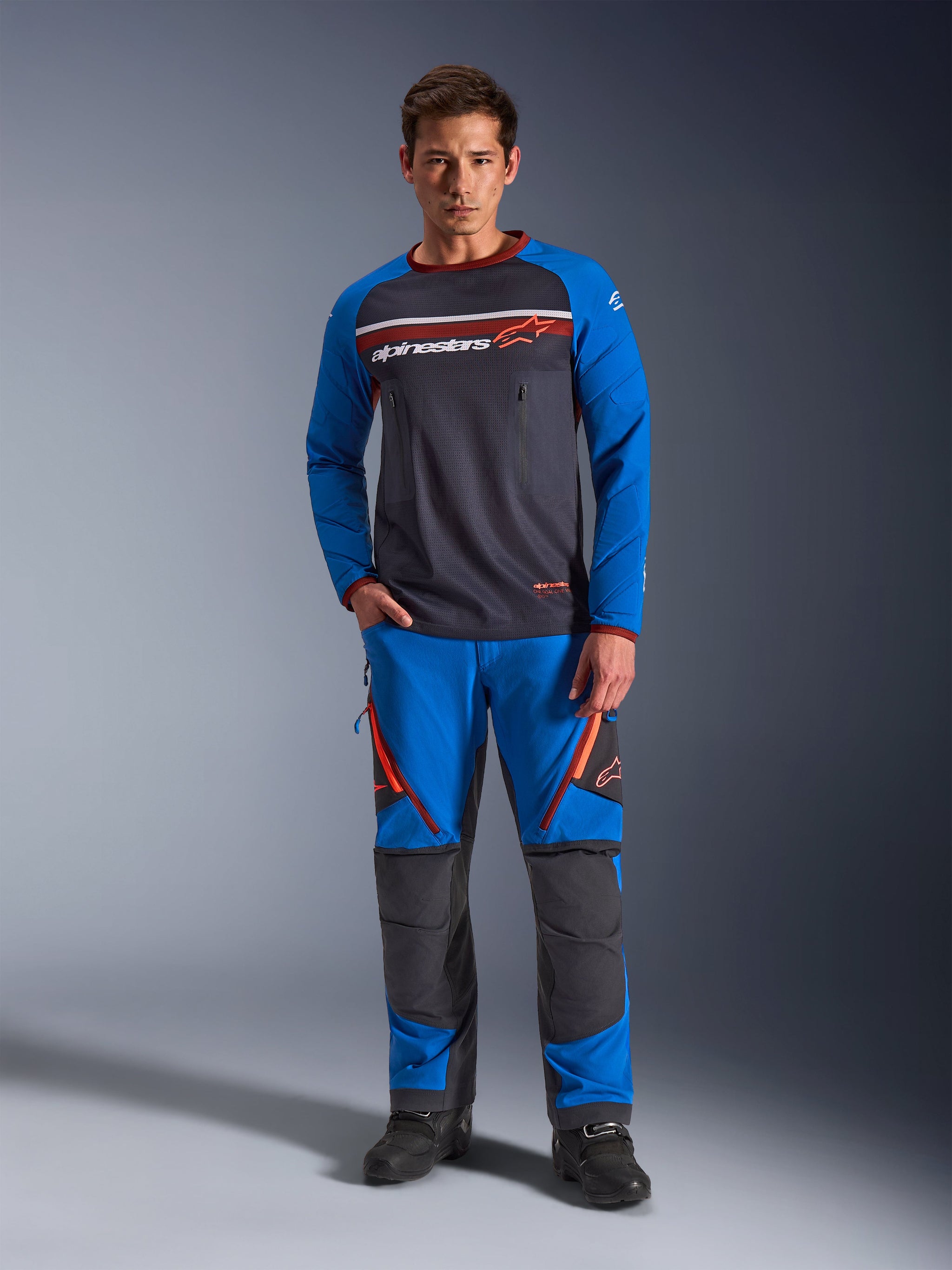 Alpinestars Maxdura Dual Jersey, Motorcycle Jersey, Deep Gray and Royal Blue, full mesh torso with padded sleeves and zippered chest pockets, featuring white and orange Alpinestars logo, worn with matching adventure pants and black boots
