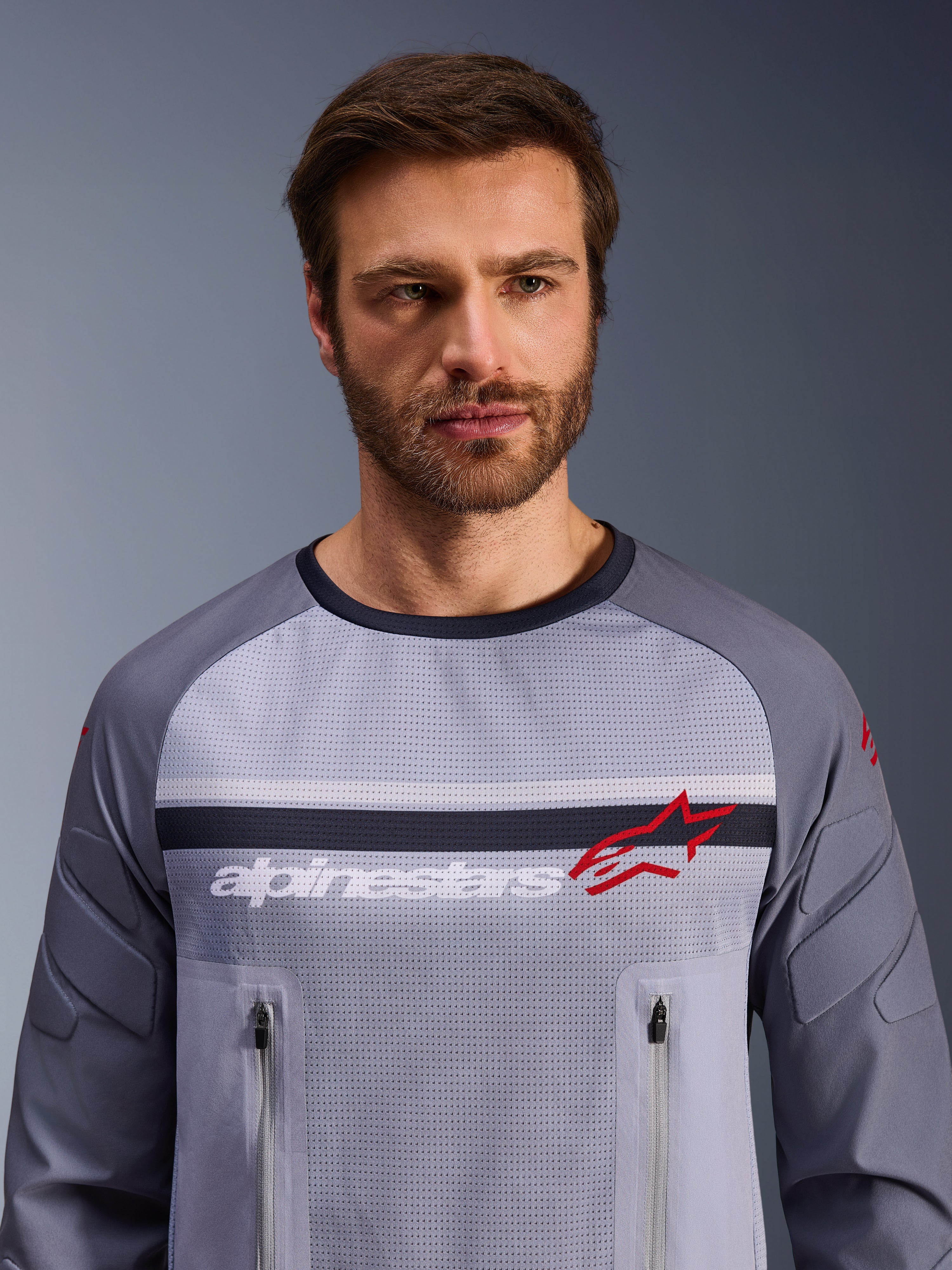 Alpinestars Maxdura Dual Jersey, Mid Gray and Dark Gray, worn by male model, featuring a mesh torso for ventilation, dual zippered chest pockets, white 'alpinestars' branding and red star logo, performance off-road adventure gear