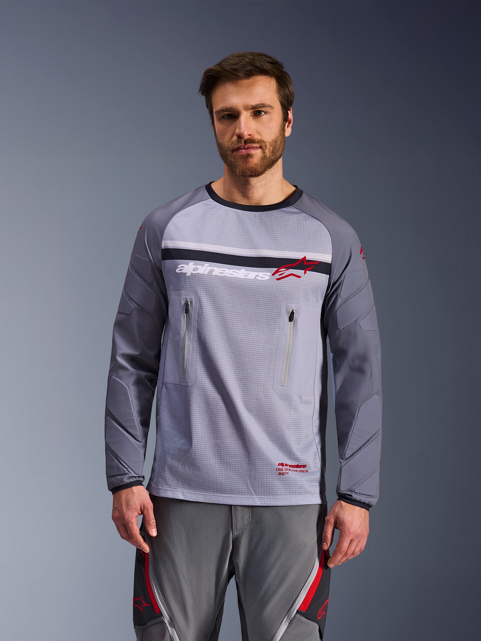 Alpinestars Maxdura Dual Jersey, Mid Gray and Dark Gray, worn by a model with matching grey pants, featuring zippered chest pockets, mesh torso construction, and padded abrasion-resistant sleeves, adventure motorcycle off-road gear
