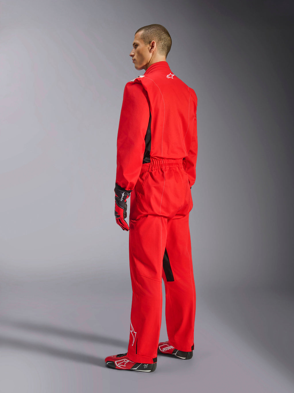 Alpinestars Kart Indoor V2 Suit, Red karting suit, rear three-quarter view on a model, worn with matching red gloves and racing shoes, single-layer poly-cotton twill construction, professional motorsport gear for indoor karting.