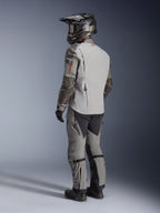 Alpinestars Nazca 3L GORE-TEX PRO Jacket, adventure motorcycle jacket in Dark Gray and Mid Gray, rear three-quarter view on model wearing full riding gear, including matching pants and helmet, technical design with Superfabric reinforcements on elbows.