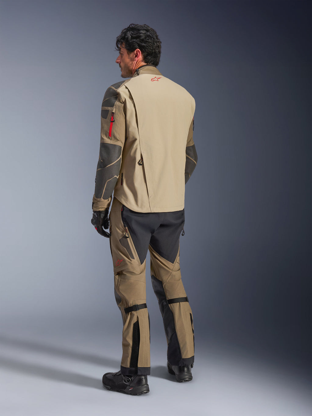 Alpinestars Nazca 3L GORE-TEX PRO Jacket, Adventure Motorcycle Jacket, Walnut Rock Brown, rear view of a rider wearing a full adventure riding outfit with matching pants and boots, featuring tan and black paneling, red logo on the upper back, durable textile construction.