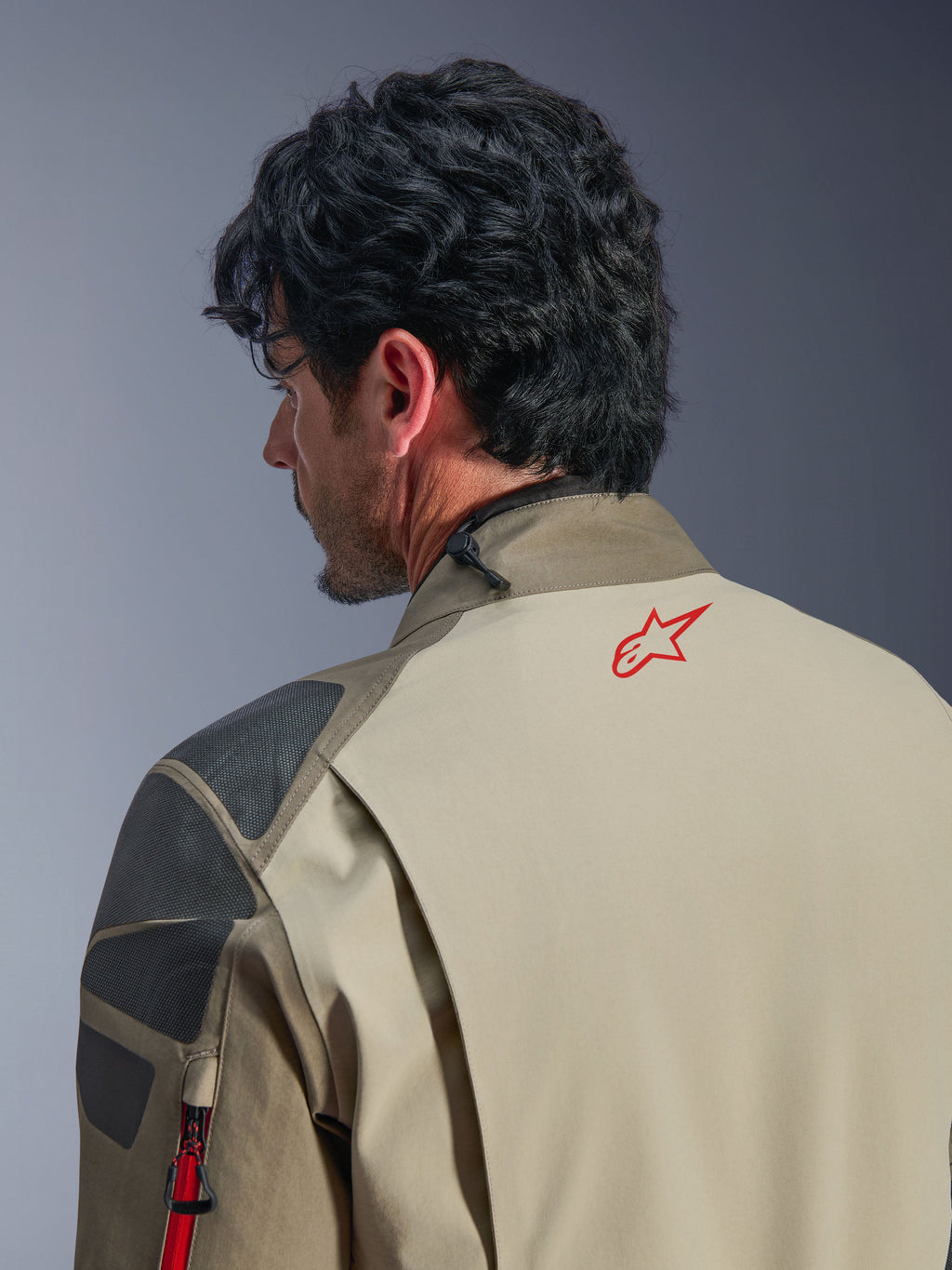 Alpinestars Nazca 3L GORE-TEX PRO Jacket, Walnut Rock Brown adventure jacket, close-up of the back and shoulder, red star logo on the neck, grey textured reinforcement panels, durable textile construction for motorcycle riding