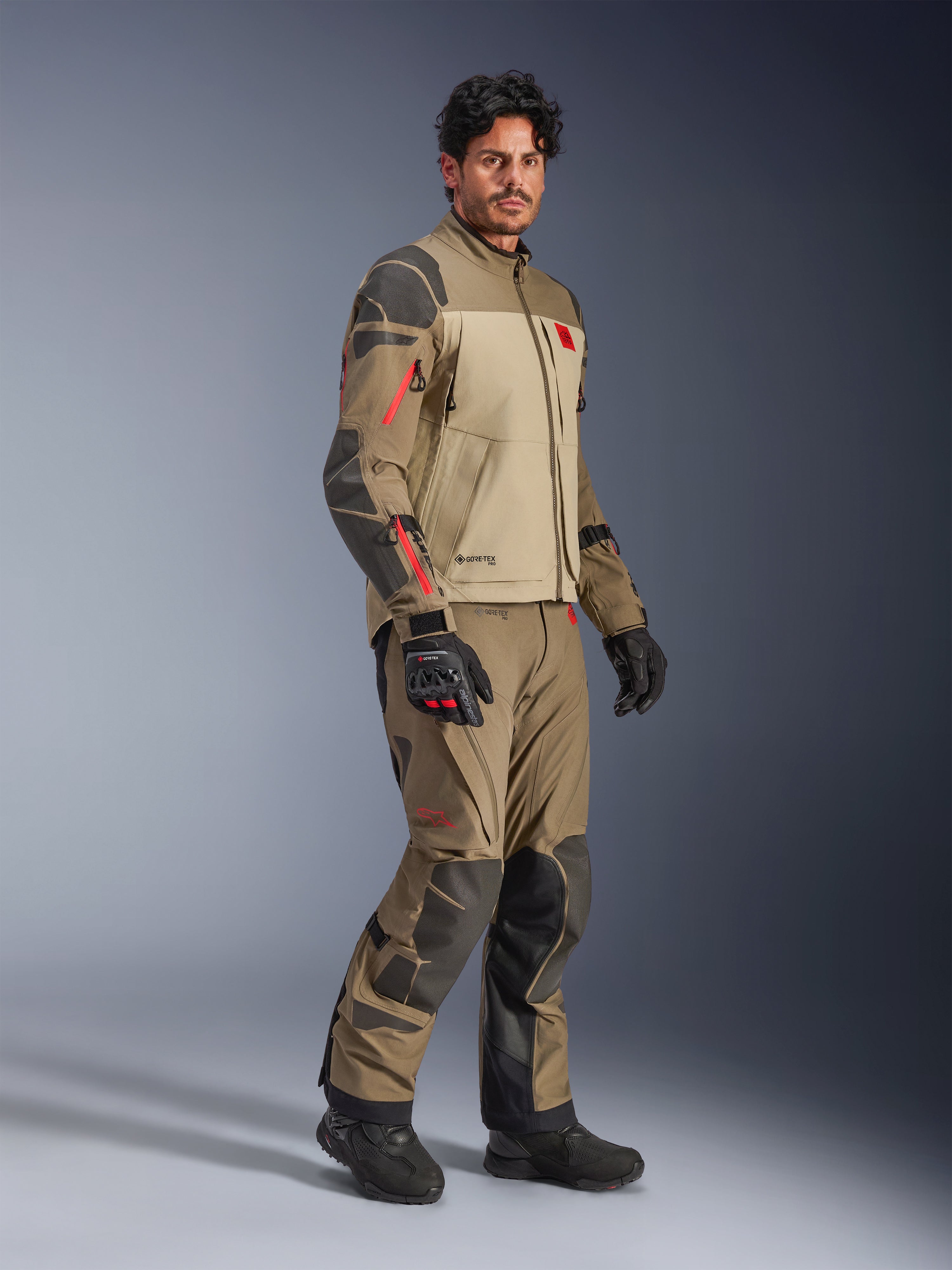 Alpinestars Nazca 3L GORE-TEX PRO Jacket, Walnut Rock Brown, adventure motorcycle riding jacket worn with matching pants and black gloves, featuring dark gray reinforcements, red zipper details, and a high-performance laminated shell.