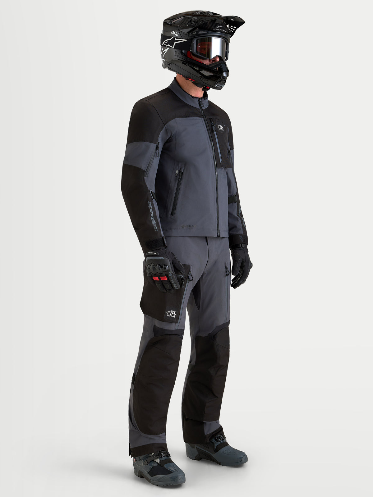 Alpinestars Arenis Gore-Tex Gear Set, men's adventure touring motorcycle jacket and pants in black and deep gray, side profile view on a model wearing matching gear and helmet, waterproof all-terrain riding apparel