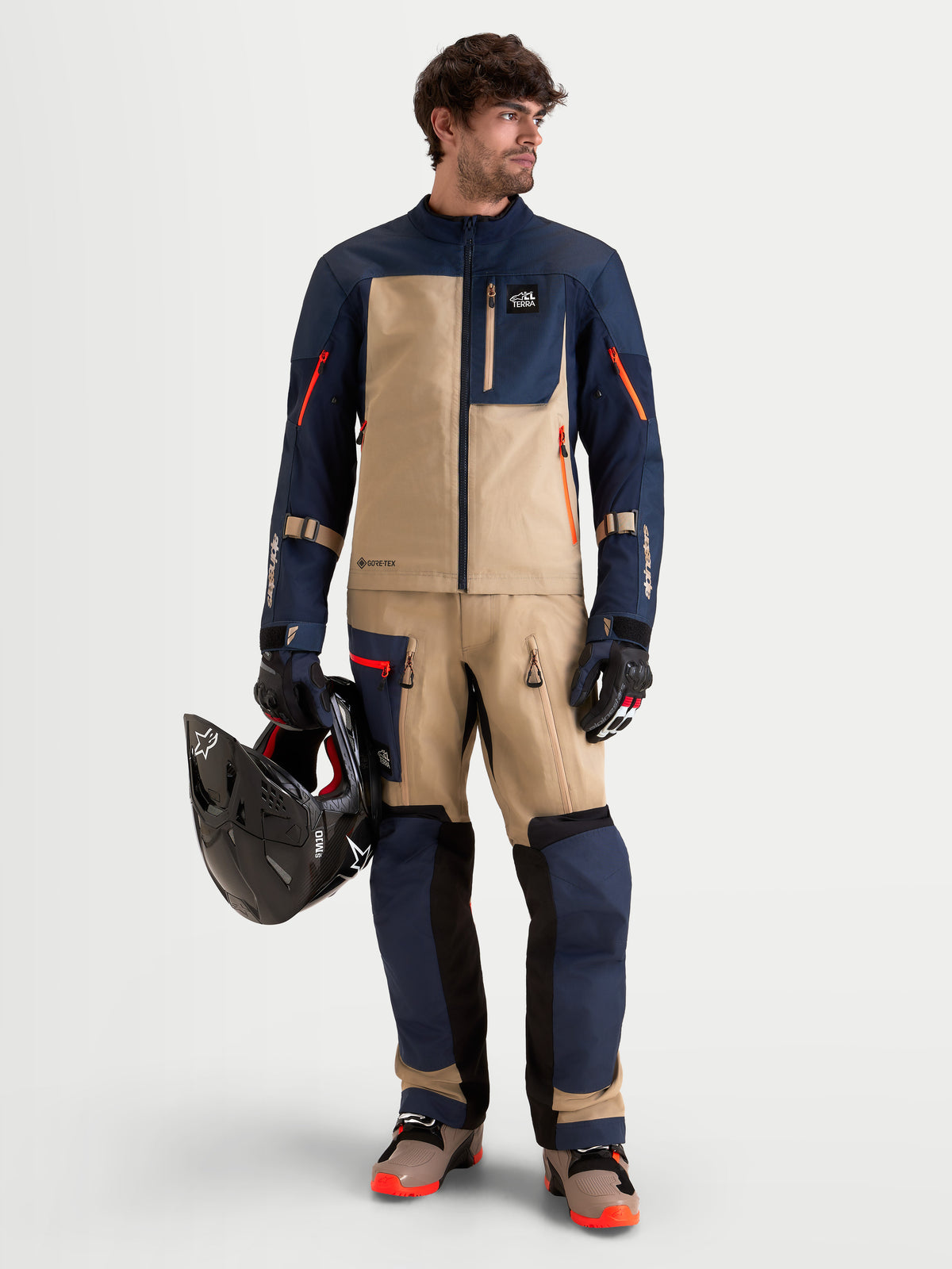 Alpinestars Arenis Gore-Tex Gear Set, men's adventure touring motorcycle jacket and pants in night navy, mood indigo, and aluminum, full-length front view on a model wearing matching gear and holding a helmet, AA certified waterproof all-terrain riding apparel.