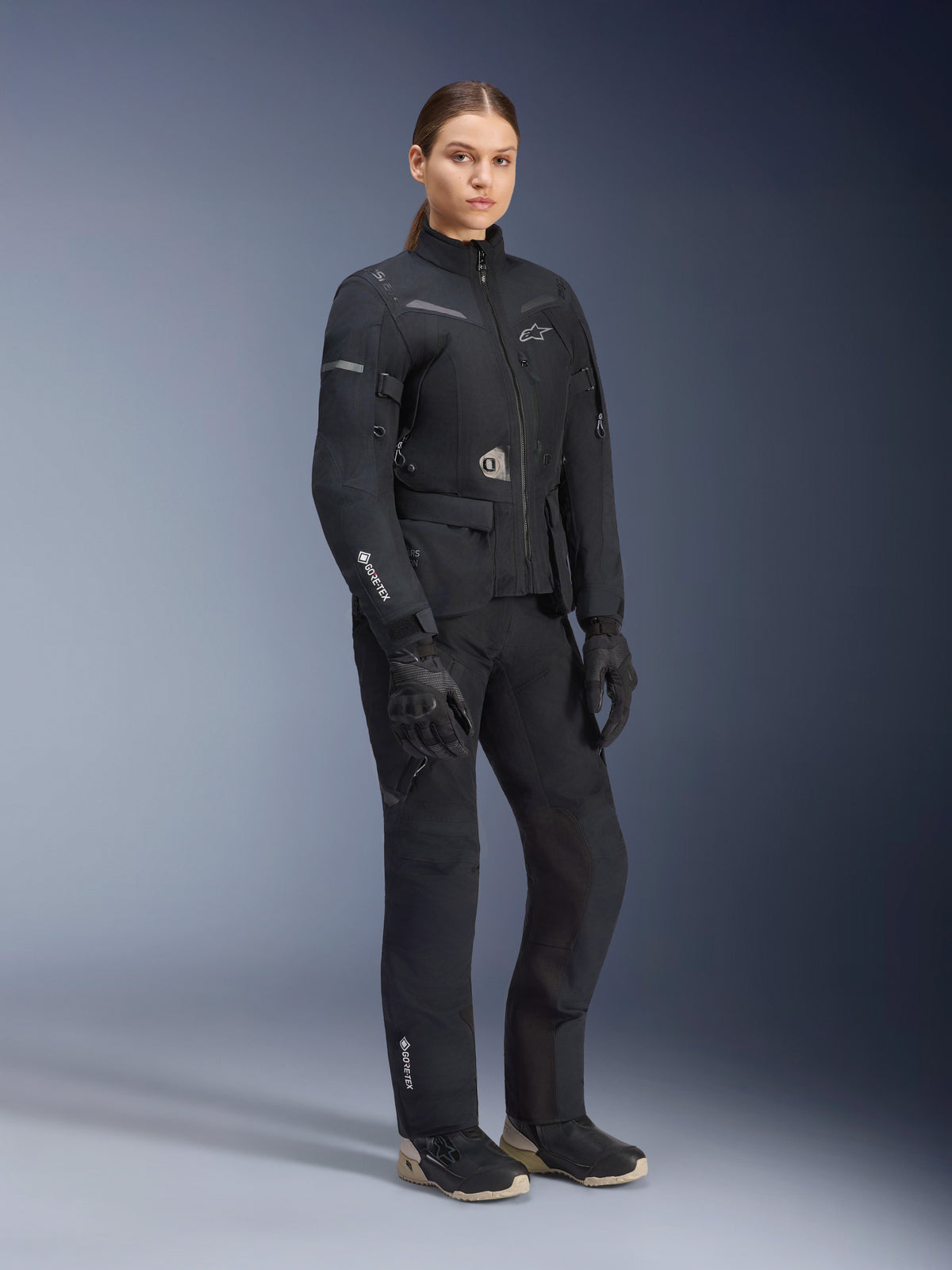 Alpinestars Women Stella ST-7 2L GORE-TEX Jacket, Black, worn with matching motorcycle pants and gloves, adventure road-touring gear with laminated GORE-TEX branding on the sleeve and a tailored women's fit.