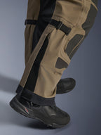 Close-up of Alpinestars Nazca 3L GORE-TEX PRO Pants in Walnut Black, showing technical details of the lower leg including calf volume adjusters and Superfabric reinforcements, worn with black adventure motorcycle boots.