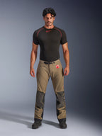 Male model wearing Alpinestars Nazca 3L GORE-TEX PRO Pants in walnut brown and black, technical adventure riding gear featuring Superfabric knee reinforcements and a magnetic waist buckle, paired with a black Alpinestars base layer shirt, studio front view.