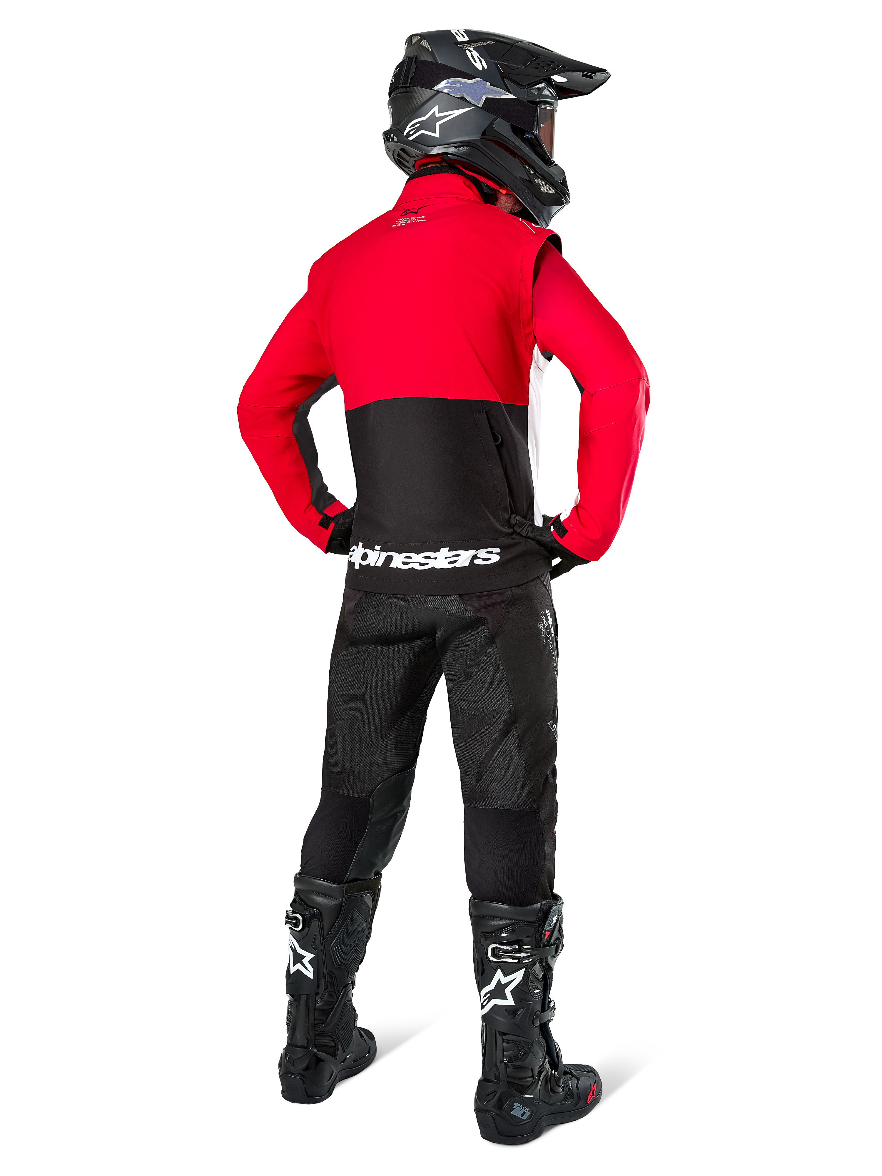 Motocross rider seen from behind wearing the Alpinestars Pro-Dura Jacket in Black, Bright Red, and White, paired with black pants, black helmet, and black off-road boots, featuring a red upper and black lower section with white Alpinestars branding across the back.