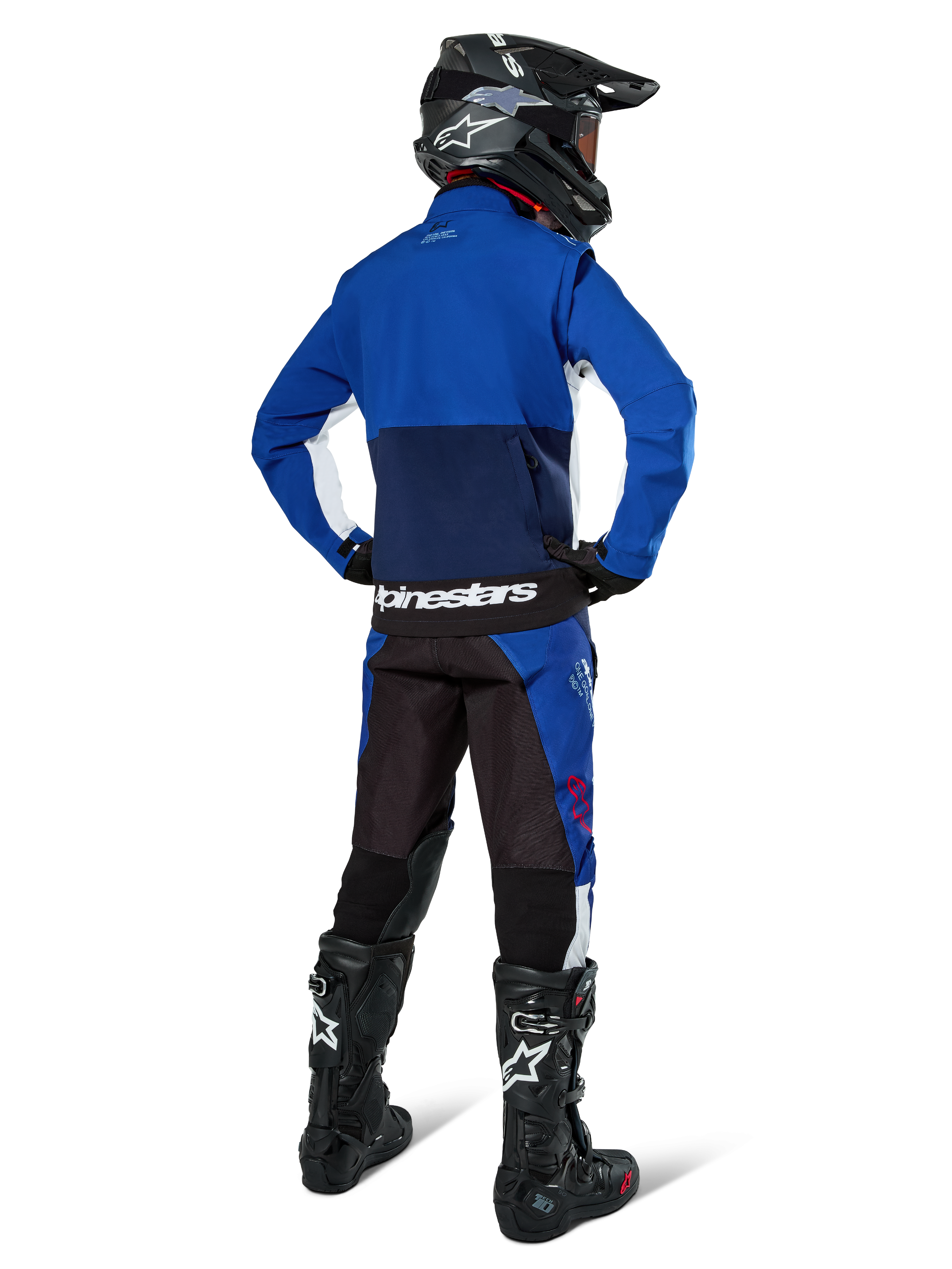 Motocross rider from behind wearing Alpinestars Lite-Dura Softshell Jacket in Navy Bright Blue and White, paired with matching enduro pants, black helmet, and black boots, complete off-road racing gear