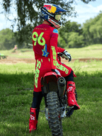Motocross rider wearing the Alpinestars 2025 Supertech Maker Gear Set in Bright Red and Yellow Fluo, sitting on a red dirt bike, featuring jersey number 96, matching red boots and helmet, professional racing gear for off-road performance