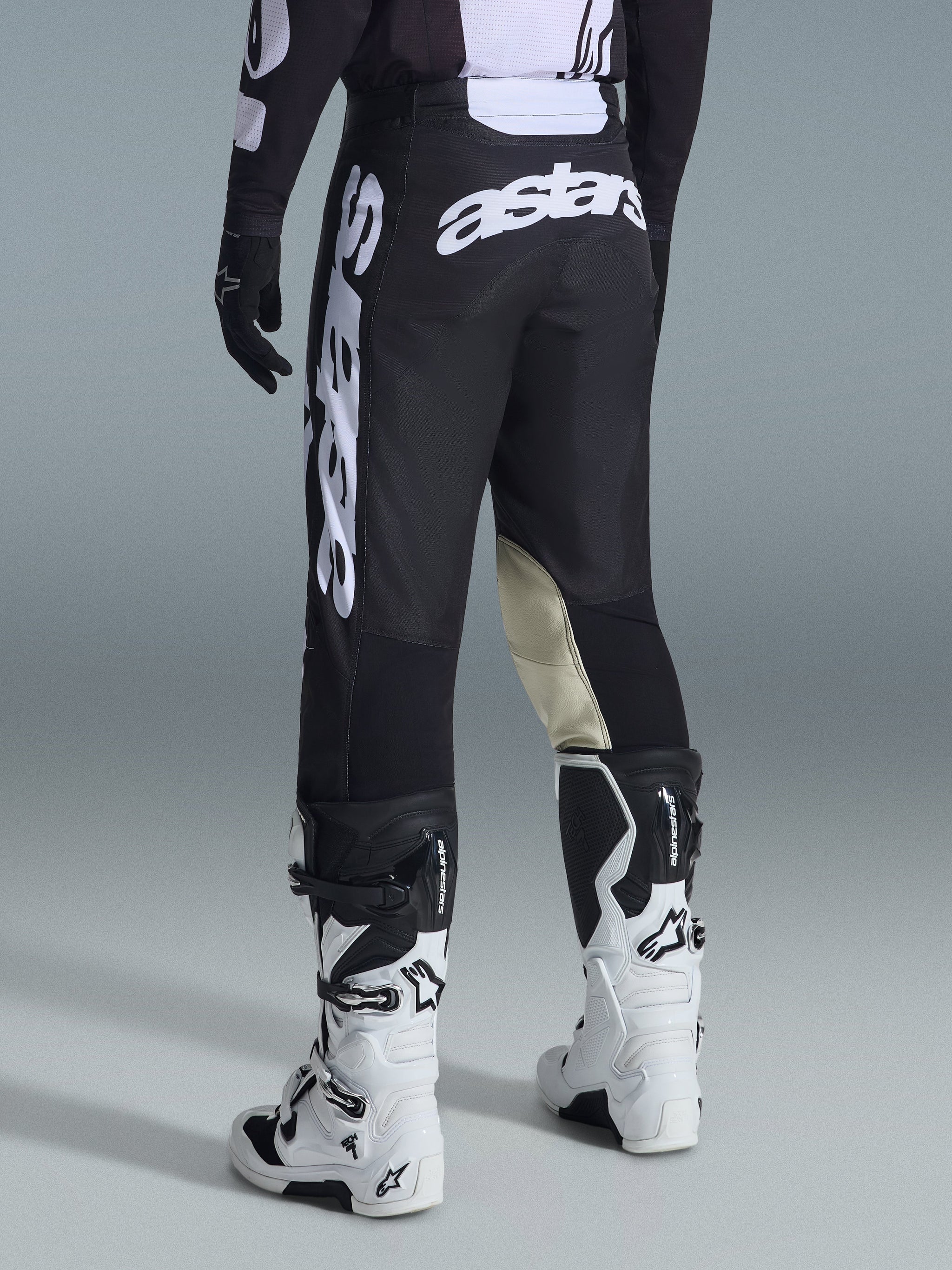 Alpinestars 2026 Racer Air Riway Pants, Motocross Pants, Black and White, rear view with large white Astars branding on seat and legs, tan leather inner knee panels, worn with white and black Tech 7 boots, premium off-road racing apparel.