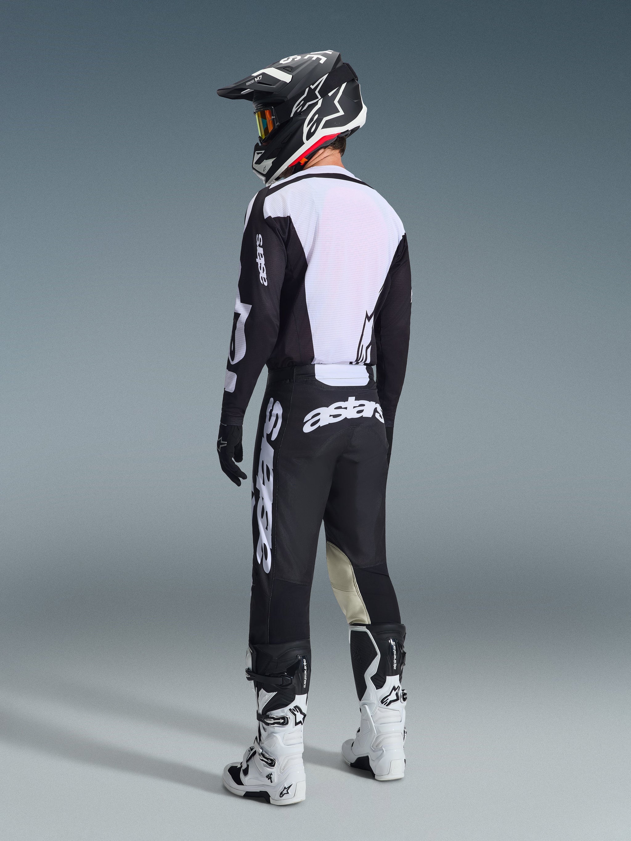 Motocross rider seen from the back wearing Alpinestars 2026 Racer Air Riway Pants in Black and White, paired with a matching ventilated jersey, black and white helmet, and white motocross boots, featuring prominent white 'astars' branding on the seat.