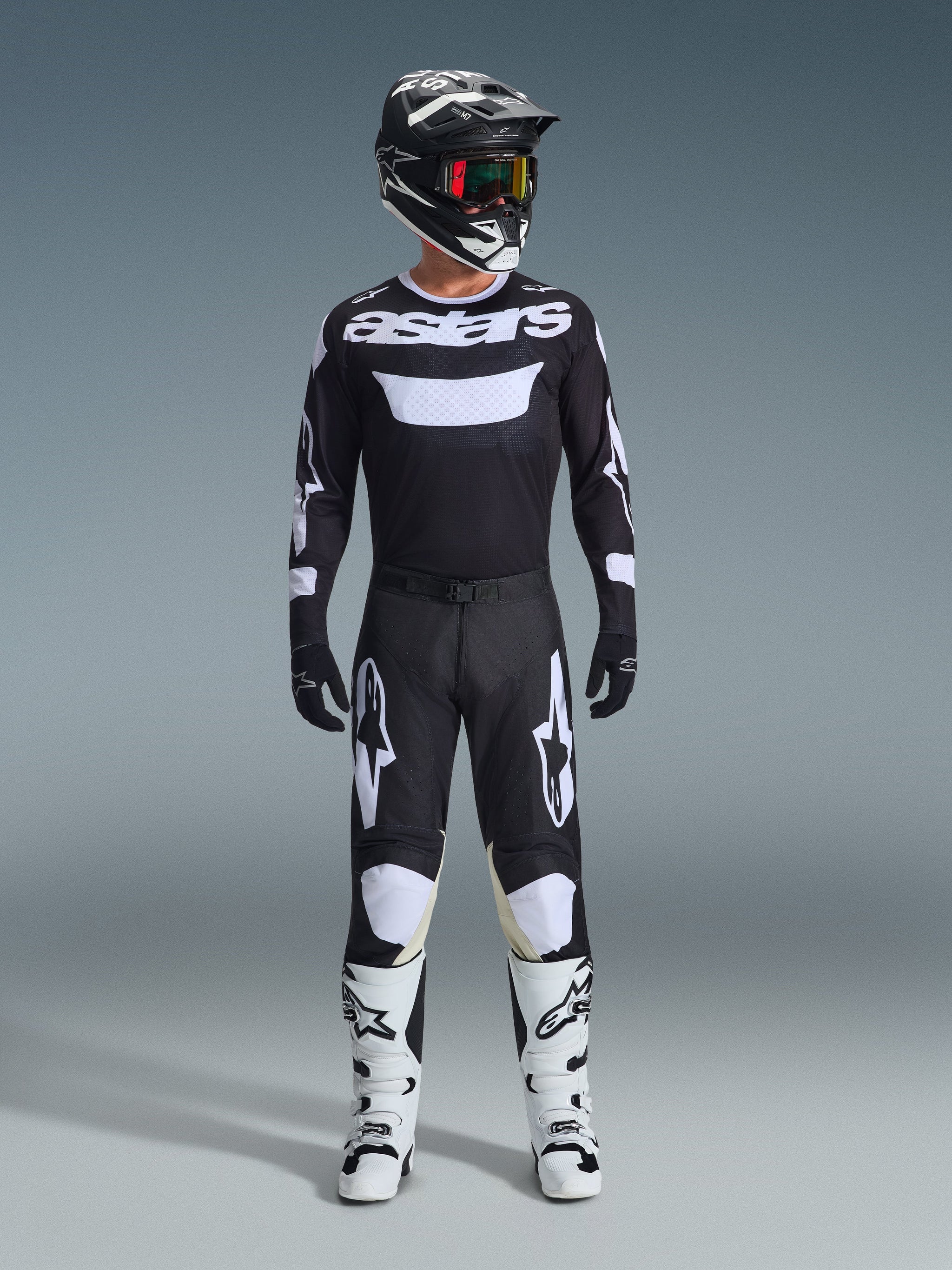 Motocross rider wearing Alpinestars 2026 Racer Air Riway Pants in Black and White, matching black and white jersey with 'astars' logo, black helmet, goggles with iridescent lenses, and white racing boots, complete professional off-road gear set