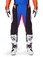 Alpinestars 2025 Techstar Melt Motocross Pants, Orange and Blue, worn with matching jersey and white boots, featuring black panels with vibrant blue and orange accents, perforated for ventilation, athletic race fit for off-road performance.