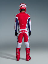 Motocross rider from behind wearing full racing gear, Alpinestars 2026 Racer Riway Pants in White Blue and Red with matching jersey, red boots and helmet, featuring large 'astars' logo on the seat, coordinated motocross outfit.