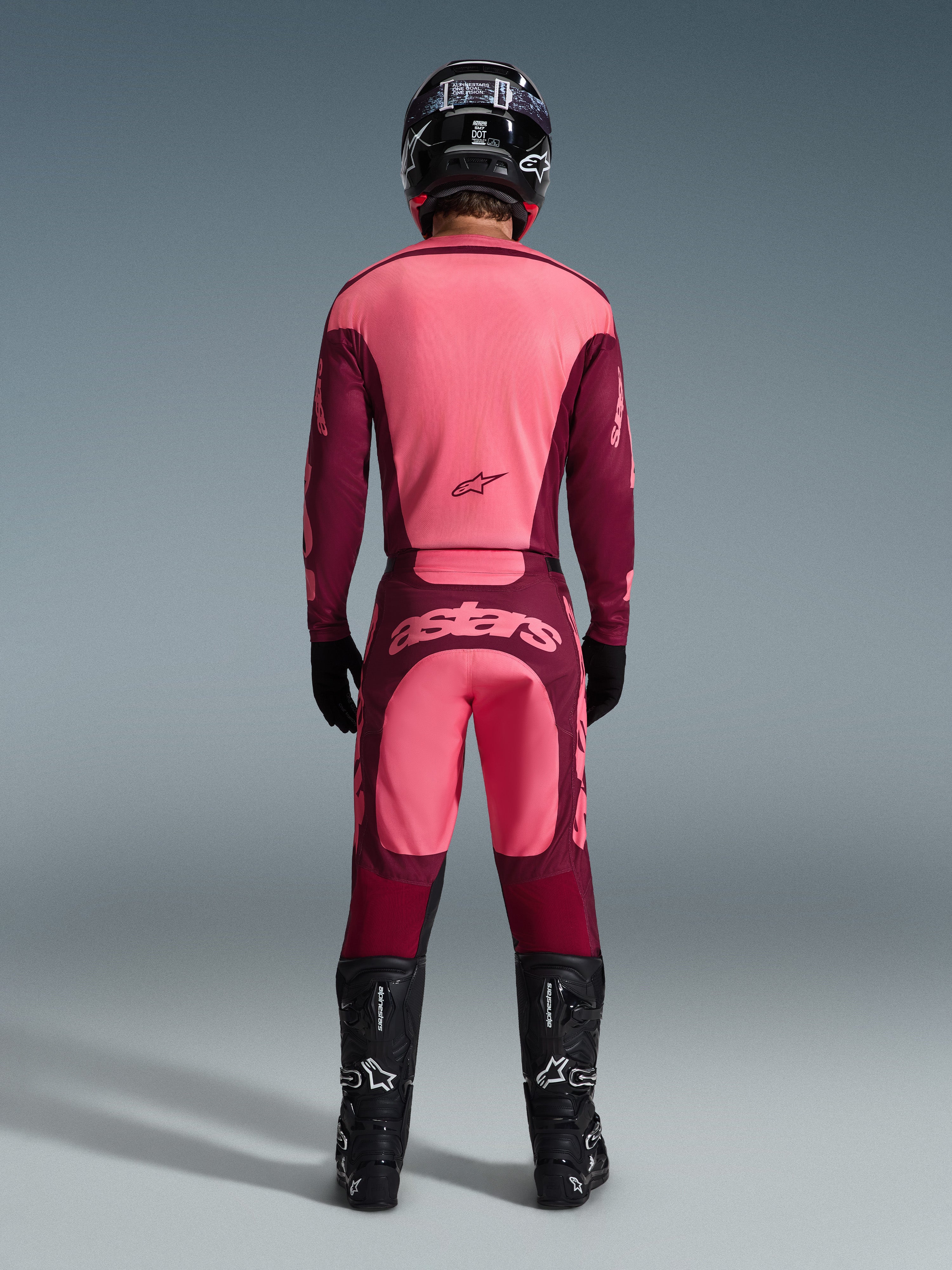 Motocross rider from the back wearing Alpinestars 2026 Racer Riway Pants in Dark Red Coral, matching jersey, black helmet, black gloves, and black Alpinestars boots, featuring a bold 'astars' logo on the seat and a two-tone red design.