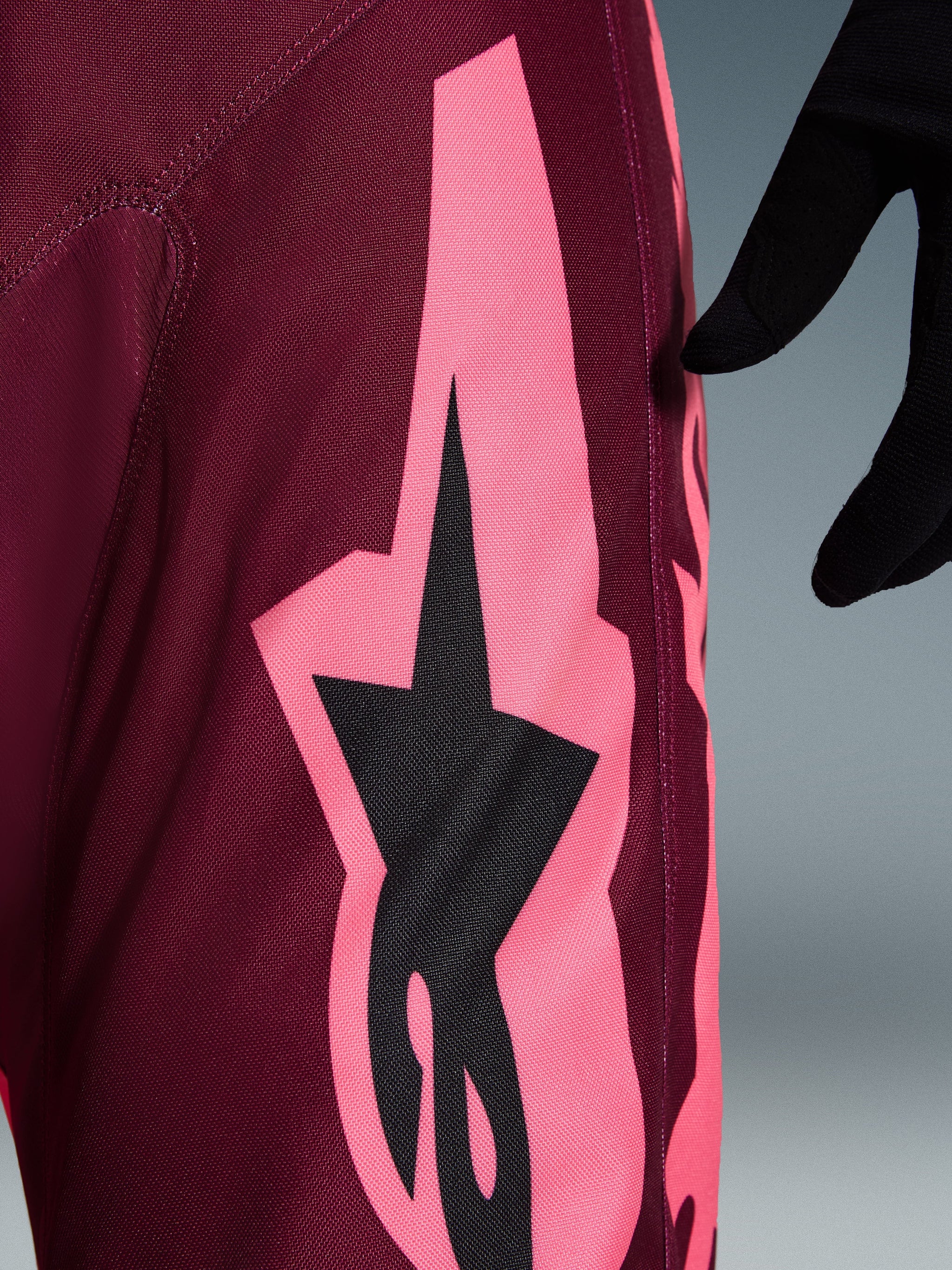 Alpinestars 2026 Racer Riway Pants, Motocross Pants, Dark Red Coral, close-up view showing a large coral pink angular graphic and black star logo, highlighting the durable polyfabric texture and performance stitching