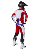 Alpinestars 2025 Racer Veil Pants, Motocross Pants, Bright Red and White with blue accents, shown from behind on a rider in full gear, featuring bold Alpinestars branding, breathable panels on lower legs, and coordinated white boots and black helmet.